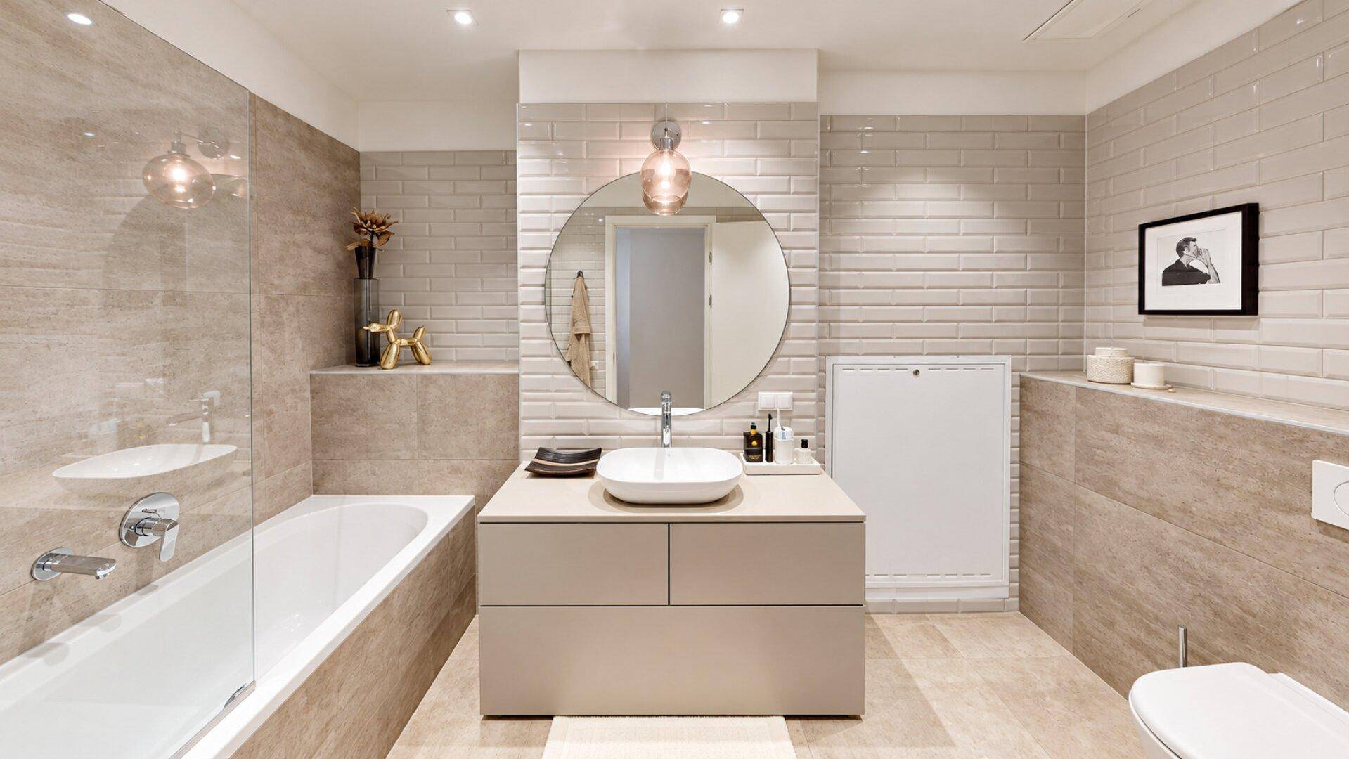 Modernes Badezimmer mit Badewanne, Einzelwaschbecken, großen Fliesen und rundem Spiegel.