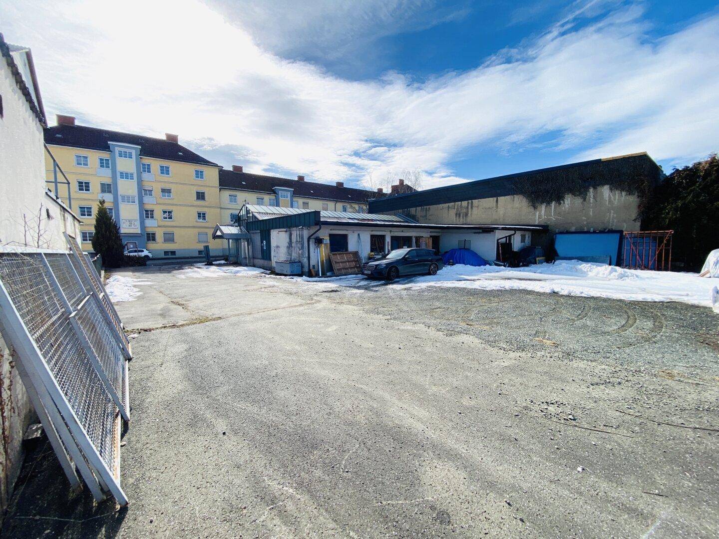 Gepflasterter Außenbereich mit Schneeresten, angrenzend an ein Gewerbegebäude und Wohnkomplexe.