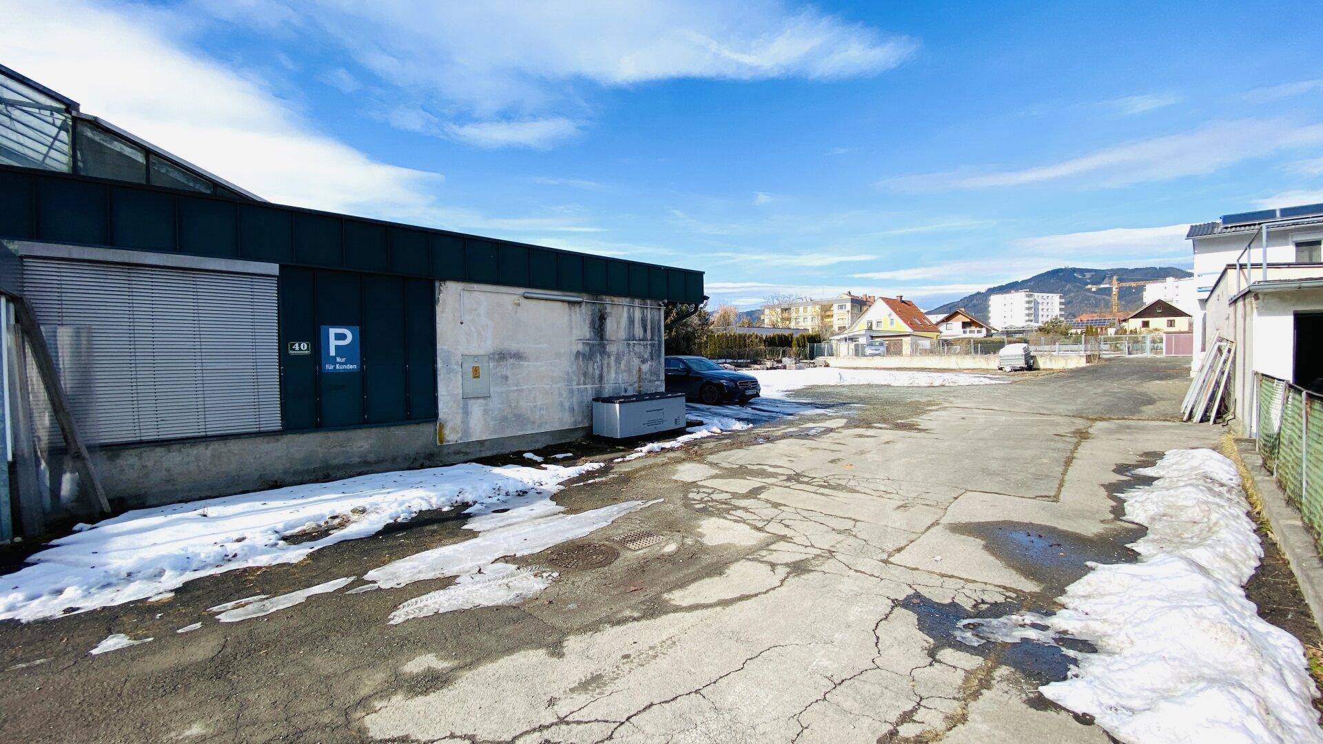 Außenansicht eines Gewerbegebäudes mit Parkplatzschild und großem, teilweise schneebedecktem Parkplatz.