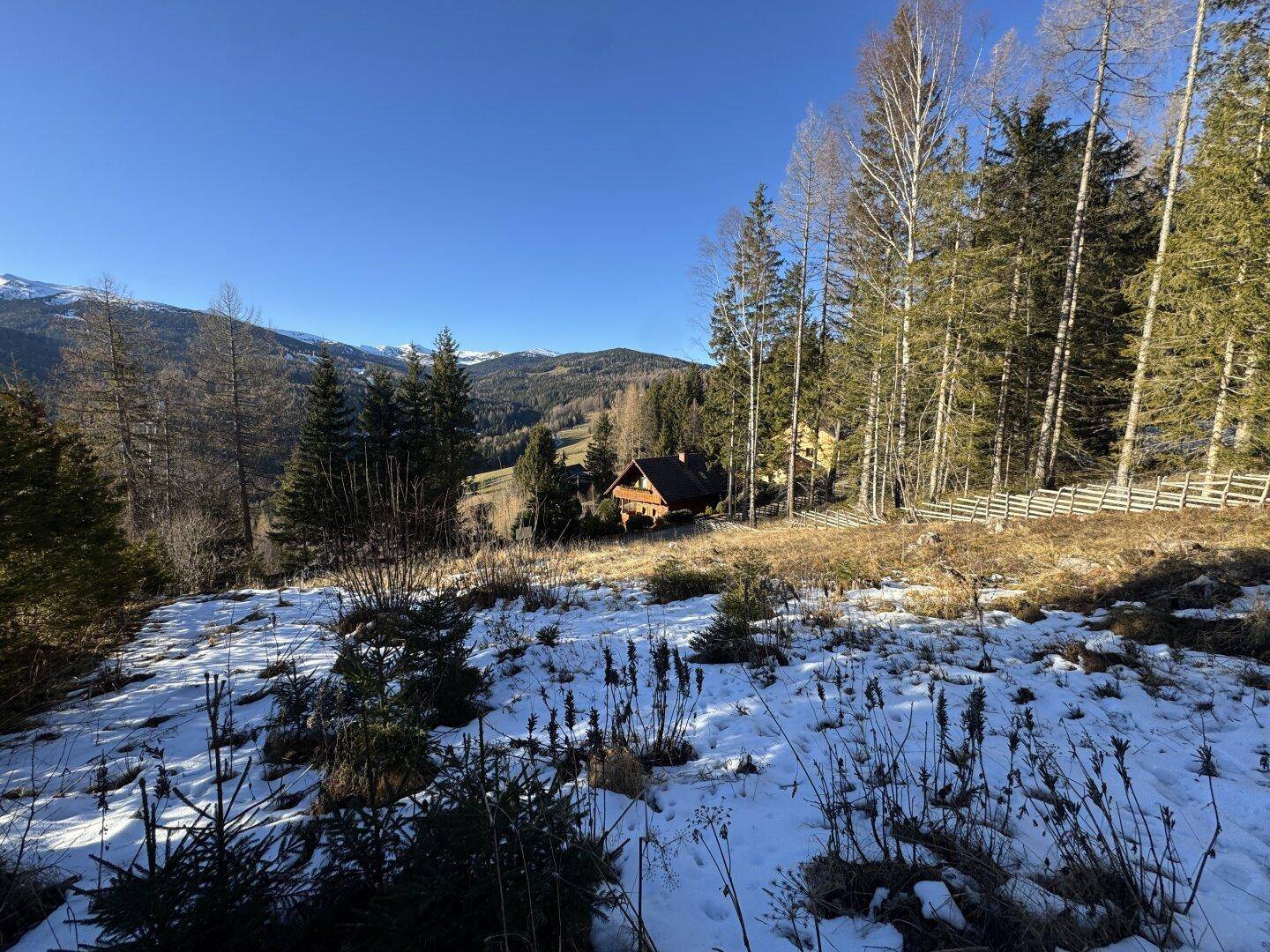 Malerische Winterlandschaft mit einem Holzhaus, umgeben von Bäumen und schneebedeckten Bergen.