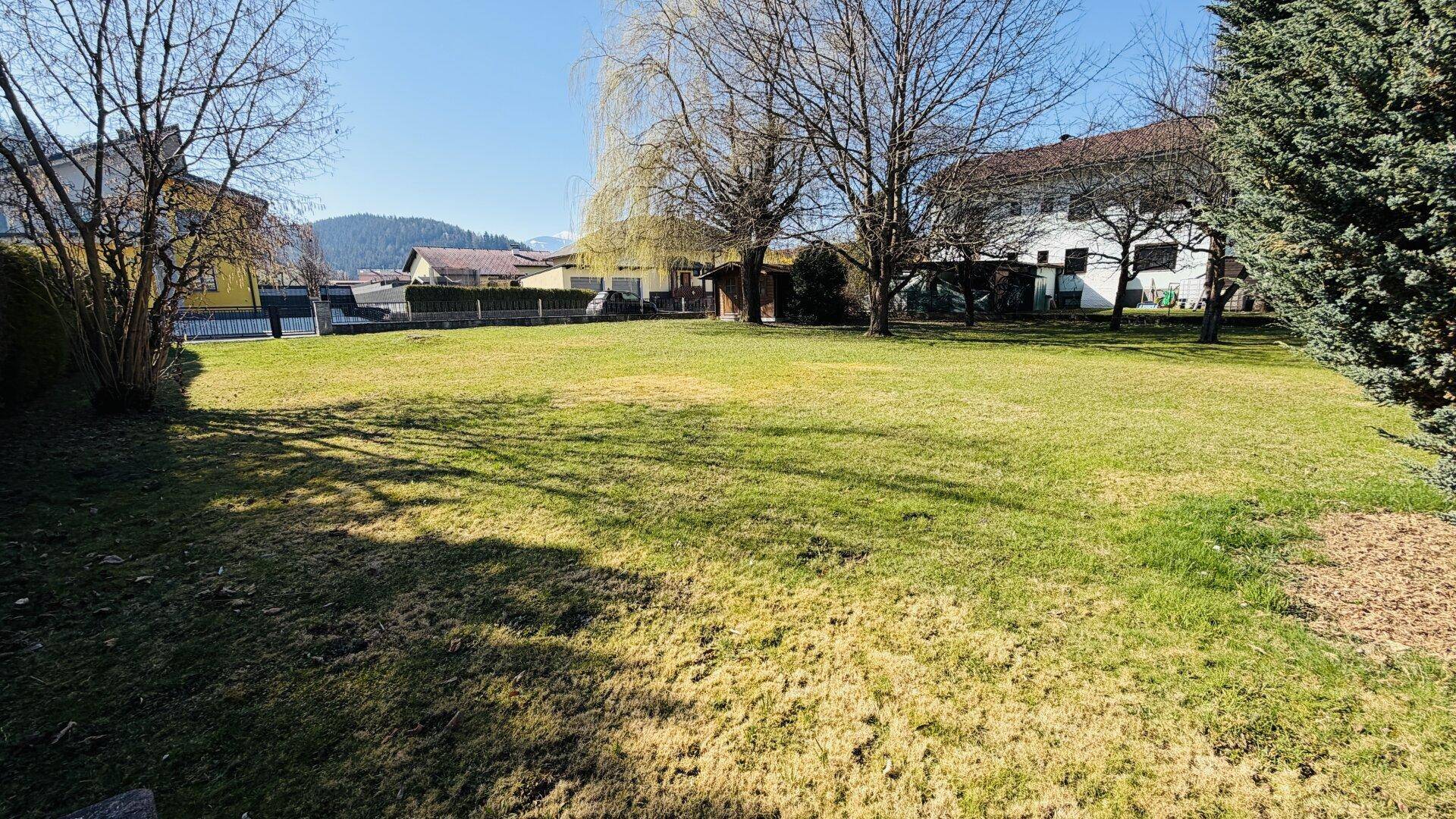 Großer Gartenbereich mit Bäumen und einer Hecke, umgeben von weiteren Wohnhäusern.