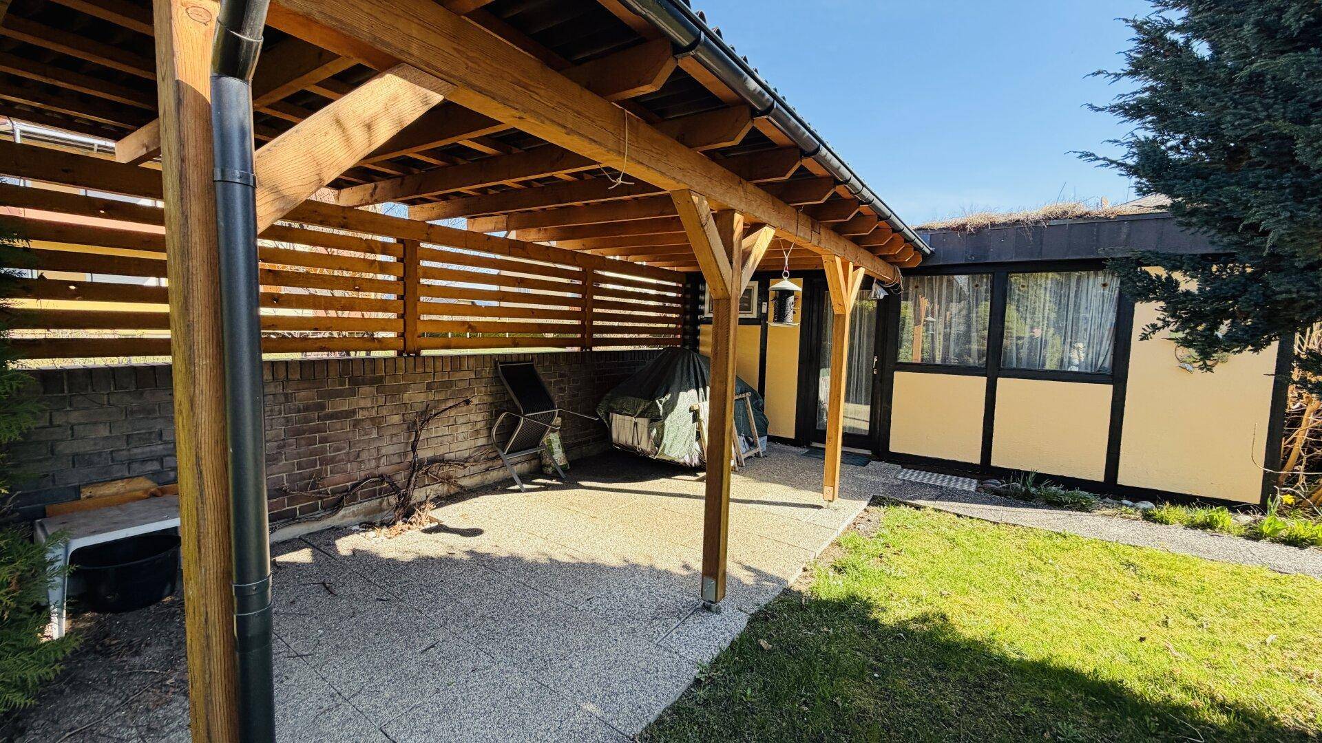 Geräumige überdachte Terrasse mit robuster Holzkonstruktion und Ziegelwand im Hintergrund.