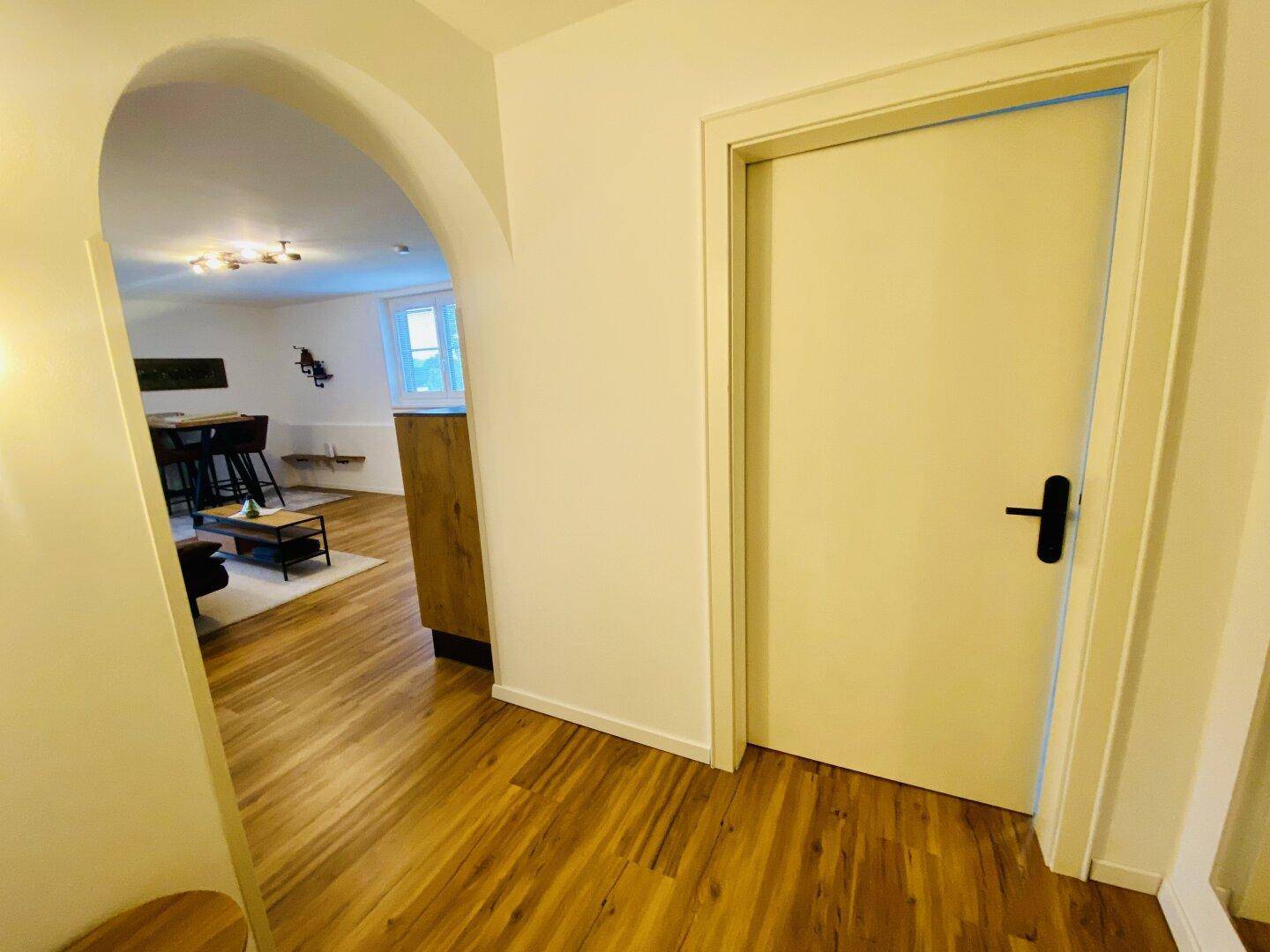 Heller Flur mit Holzboden und einem Bogen, der zum Wohnbereich führt.