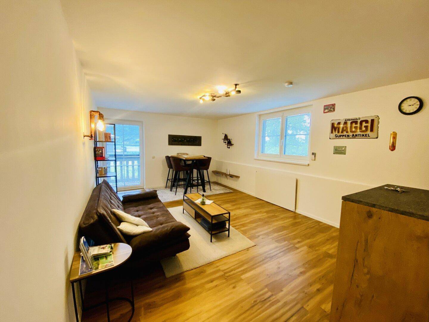 Geräumiger Wohn- und Essbereich mit Holzboden, bequemer Couch und Esstisch am Fenster.