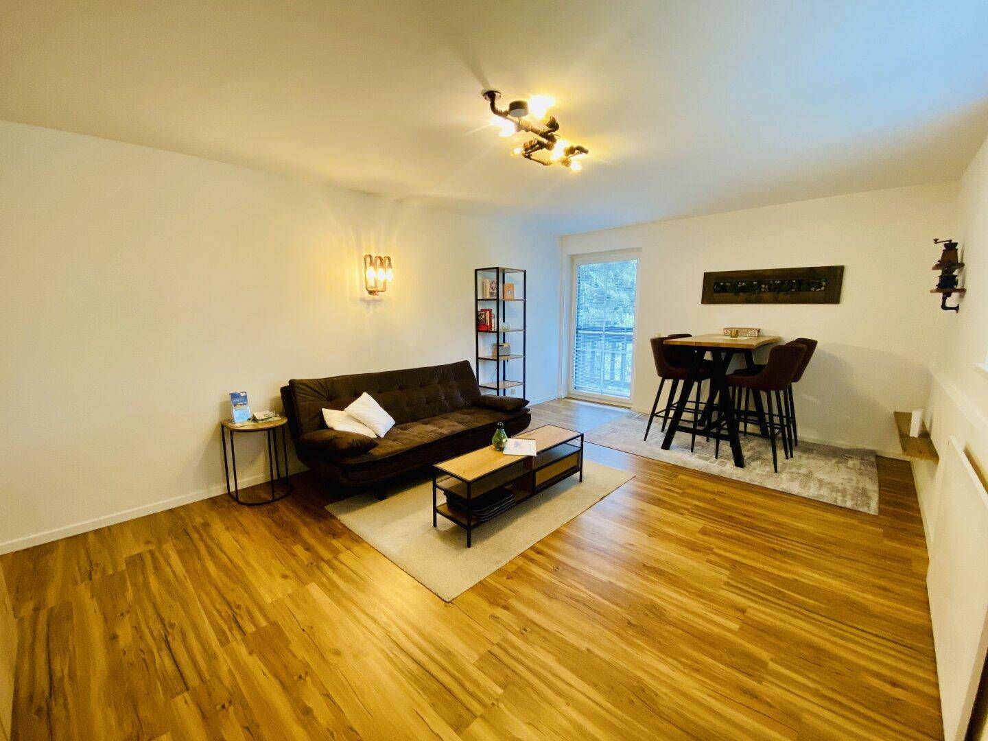 Gemütlicher Wohn- und Essbereich mit Holzboden, Sofa und Esstisch, hell beleuchtet.