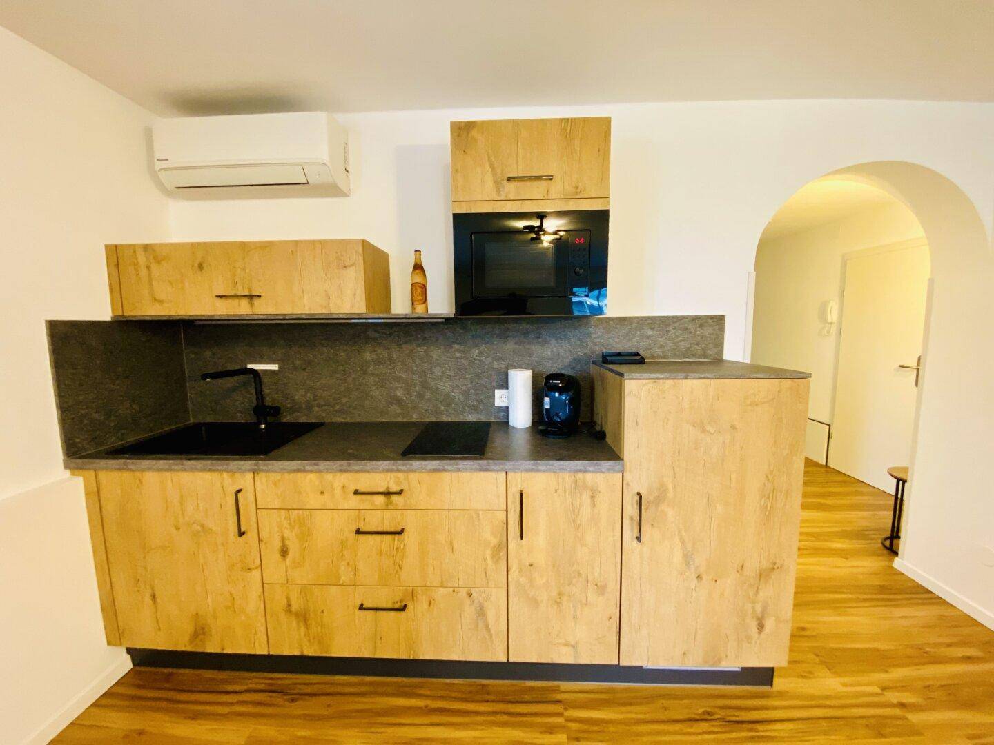 Moderne Küchenzeile mit Holzfronten, dunkler Arbeitsplatte und integrierten Geräten.