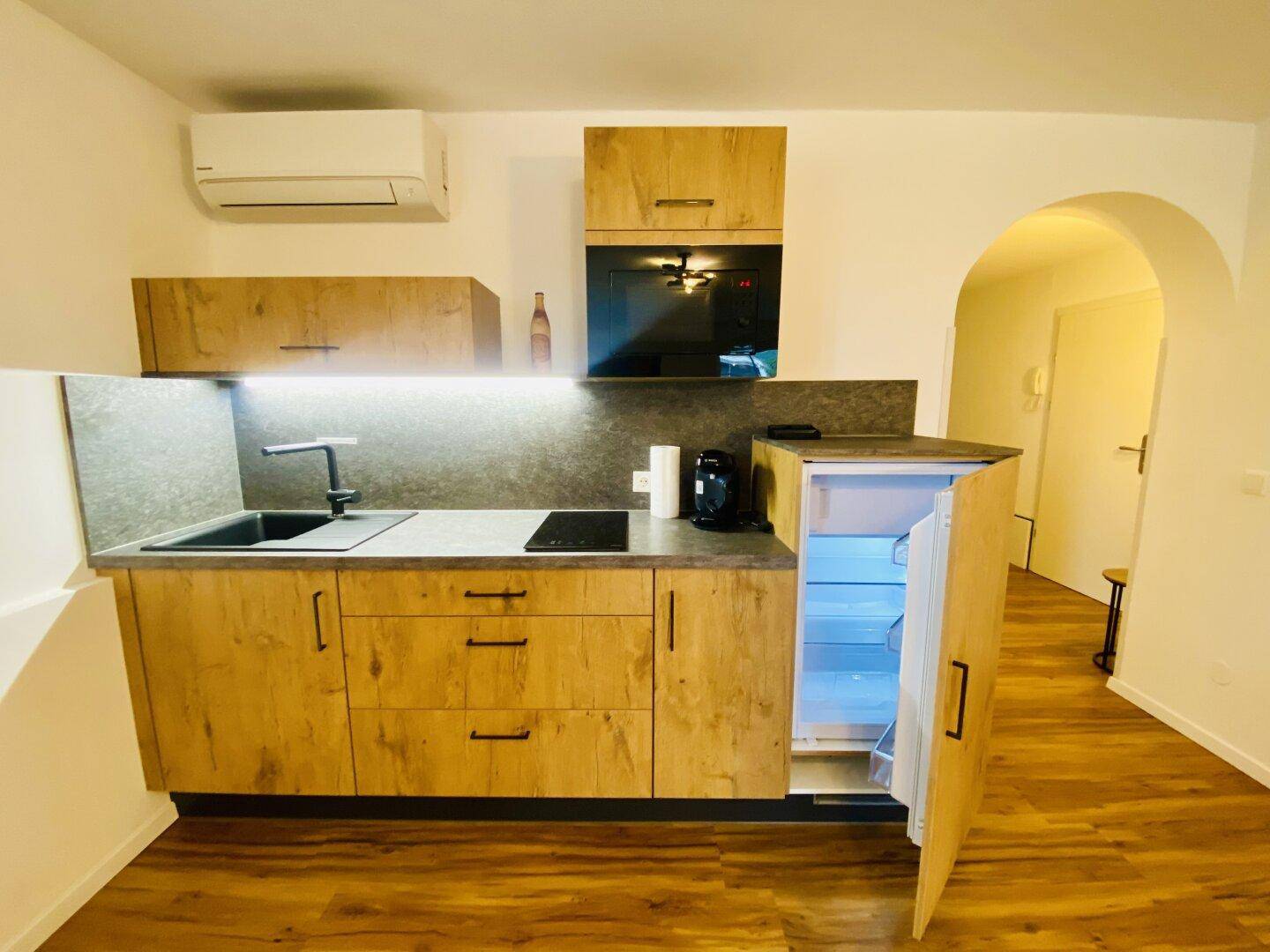 Funktionale Küchenzeile mit Holzschränken, Induktionskochfeld und Kühlschrank.