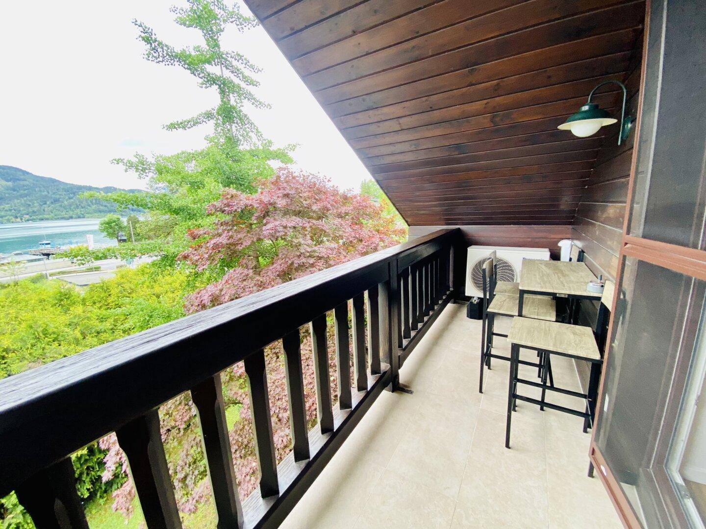 Gemütlicher Balkon mit Holzboden, Sitzgelegenheiten und weitem Blick auf den See.
