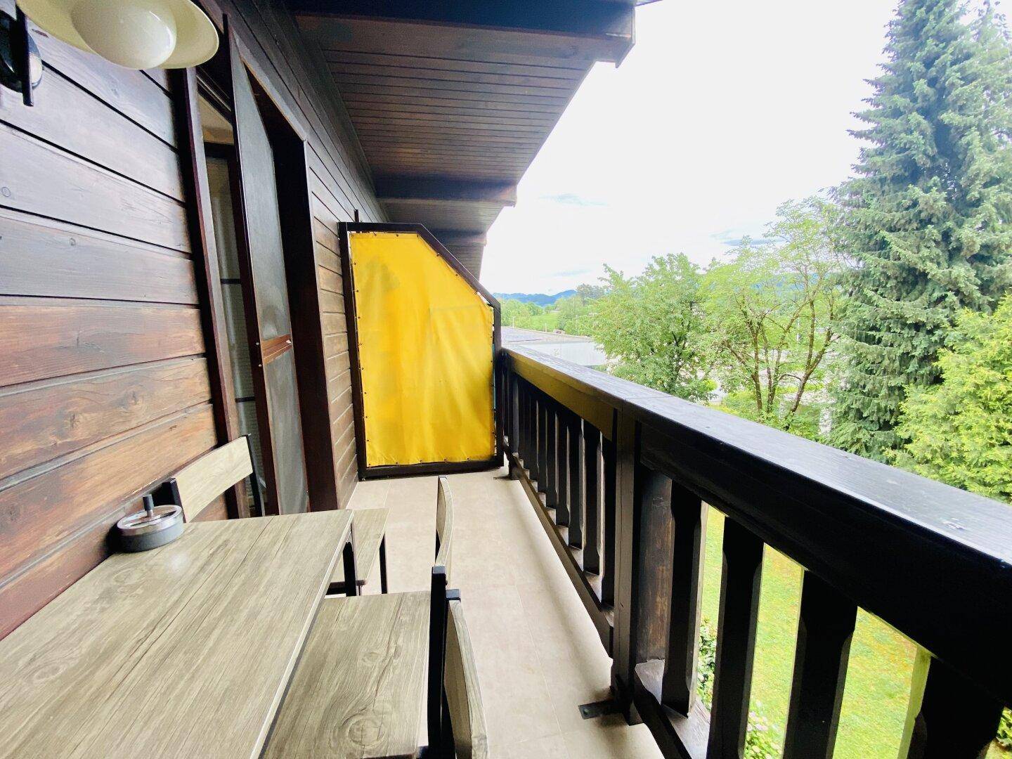 Balkon mit Holzboden und Sitzgelegenheiten, bietet einen Blick auf die grüne Umgebung.