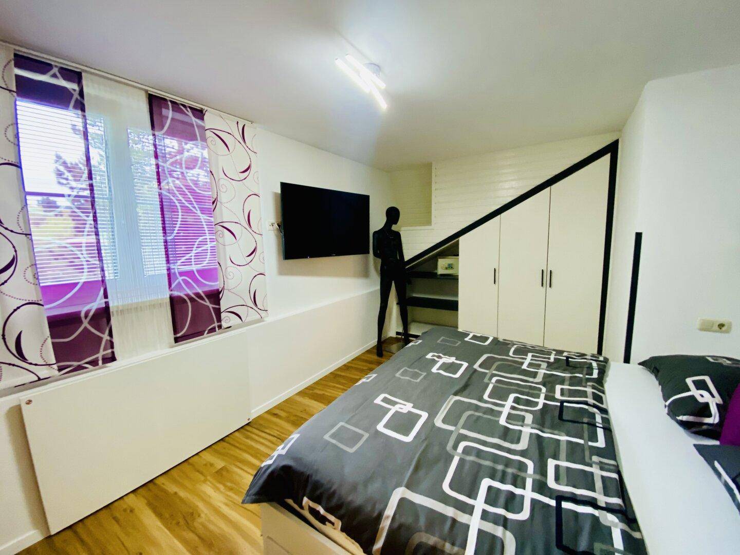 Modernes Schlafzimmer mit Holzboden, großem Bett, Wandfernseher und Einbauschränken.