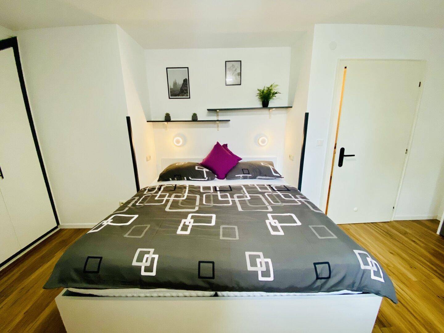 Schlafzimmer mit Holzboden, großem Bett, Wandregalen und moderner Dekoration.