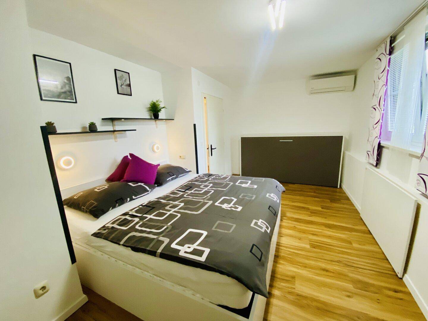 Schlafzimmer mit Holzboden, Doppelbett, Wandbett und Klimaanlage.