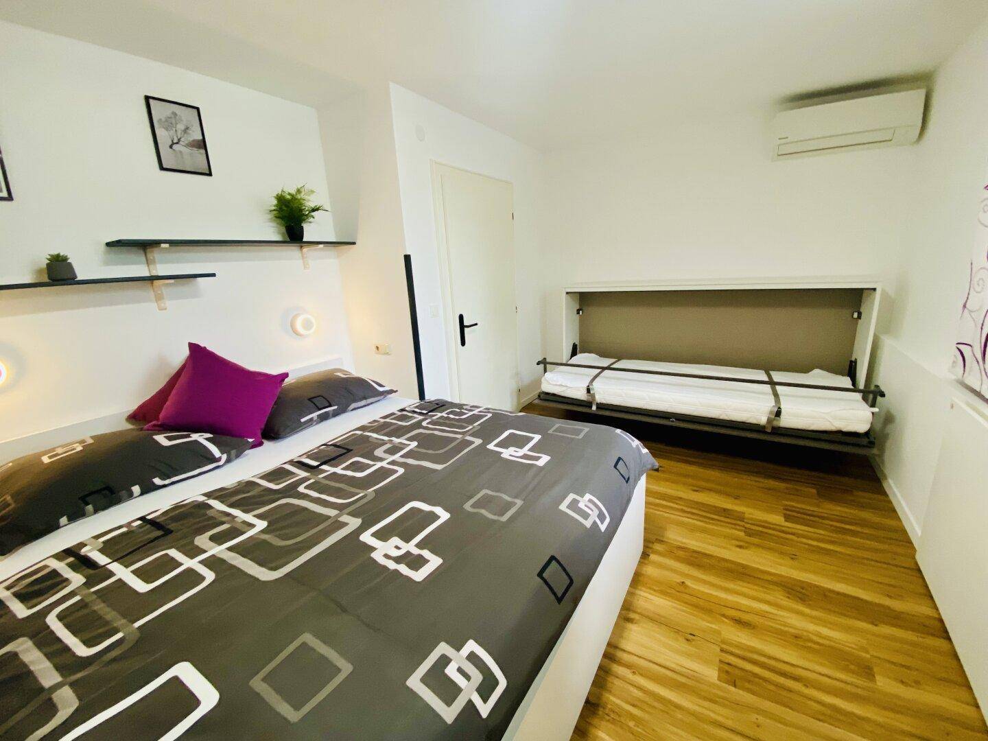 Schlafzimmer mit Holzboden, Doppelbett und einem praktischen Wandklappbett.