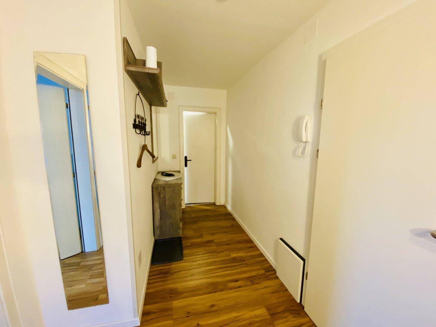 Heller Flur mit Holzboden, Spiegel und einer Ablagefläche an der Wand.