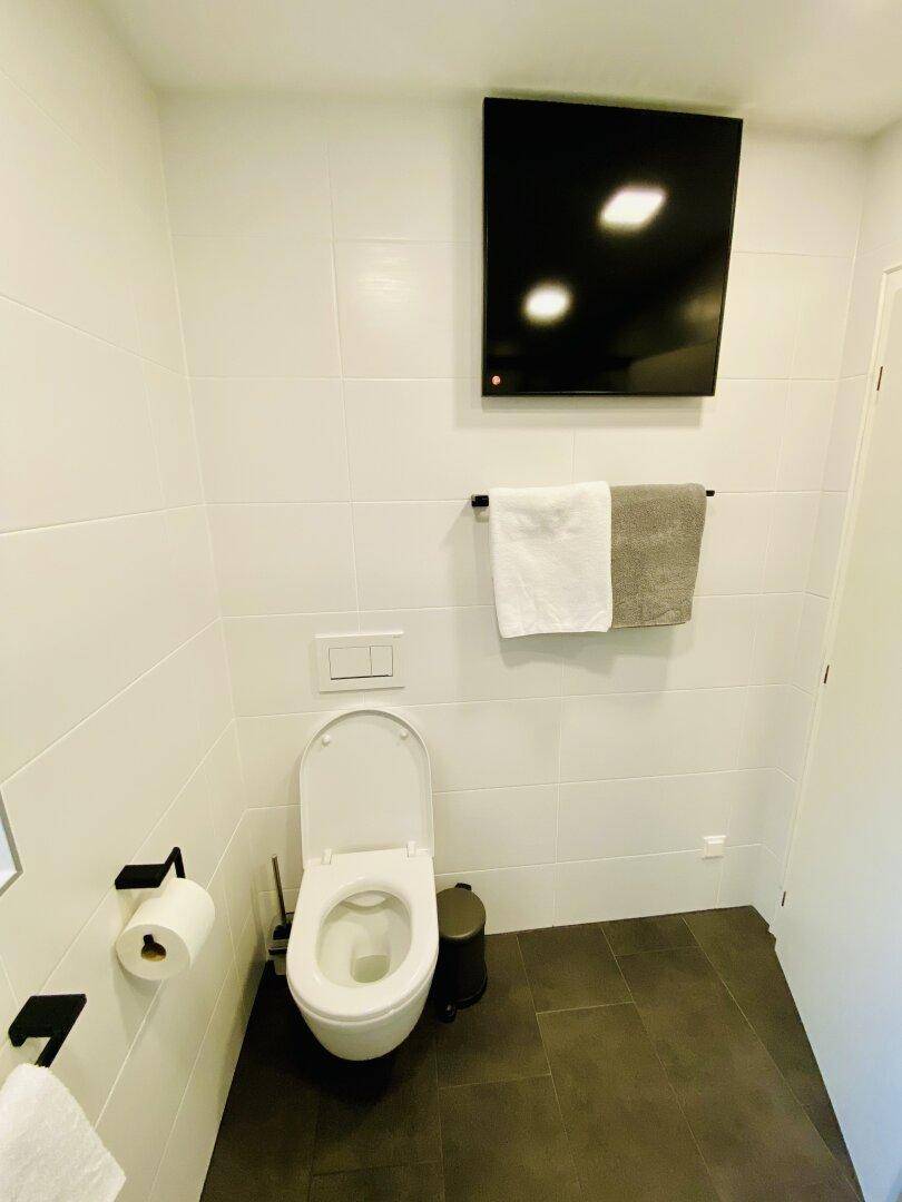 Separates WC mit wandhängender Toilette und dunklen Bodenfliesen.