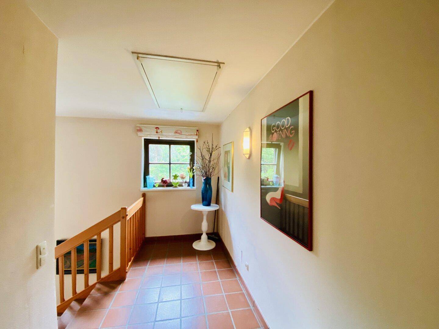 Heller Flur mit Terrakotta-Fliesenboden, Holzgeländer und Fenster.