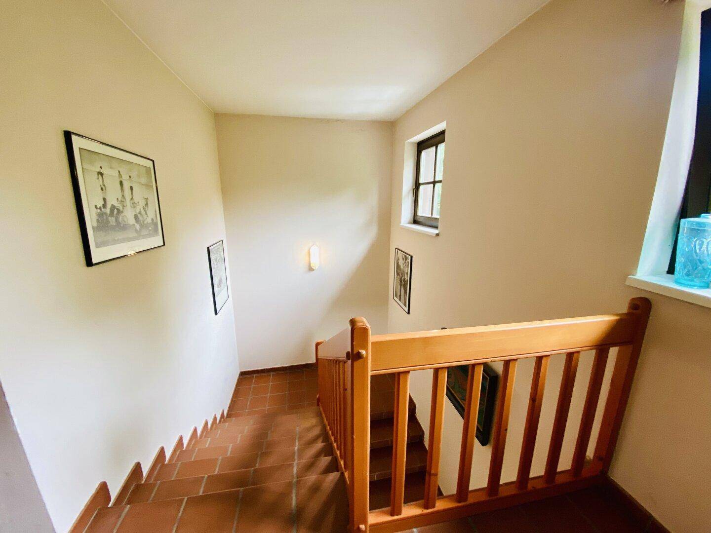Treppenhaus mit Holzgeländer, Terrakotta-Fliesen und natürlichem Lichteinfall.