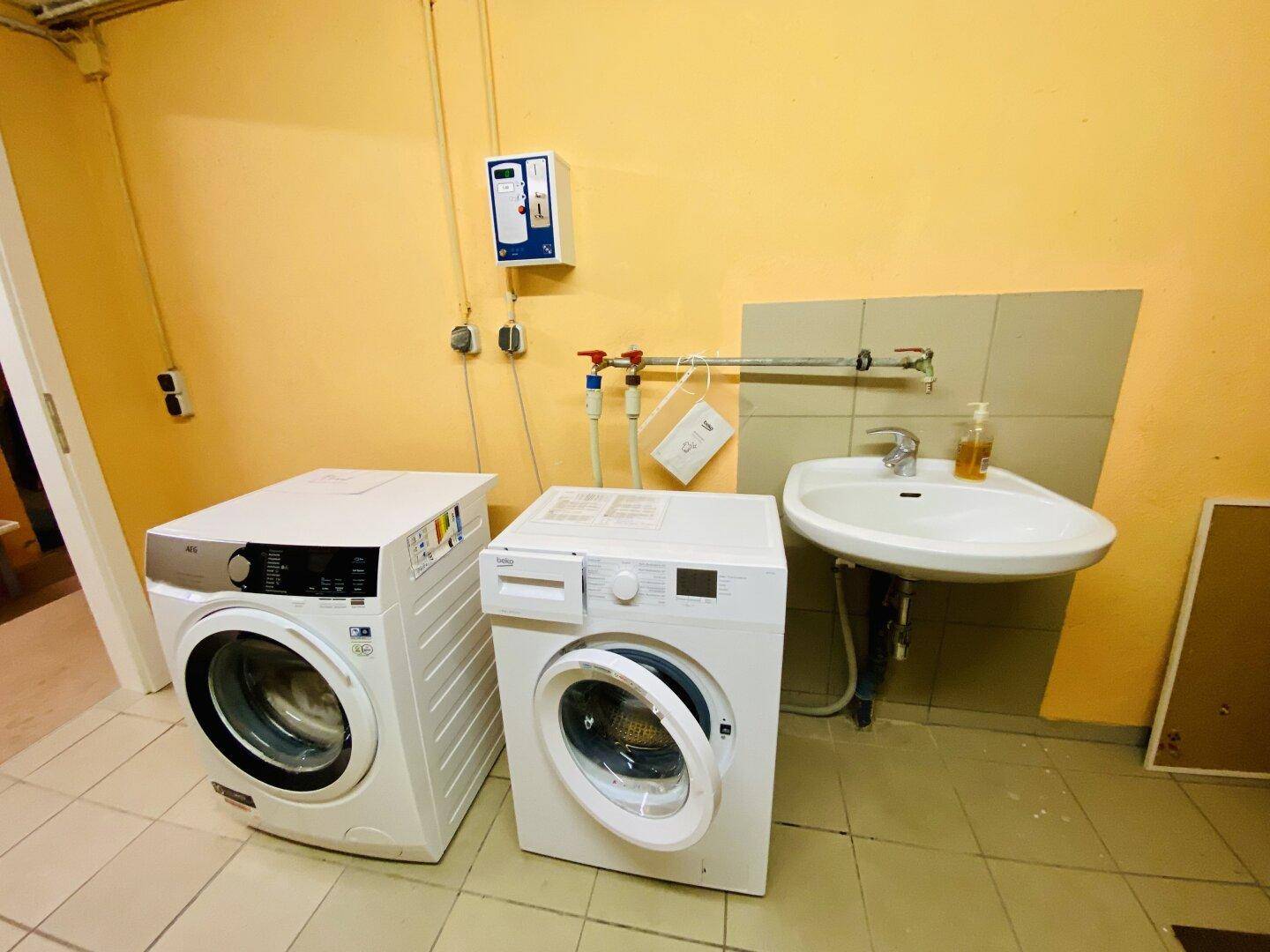 Waschküche mit zwei Waschmaschinen, Waschbecken und gelben Wänden.