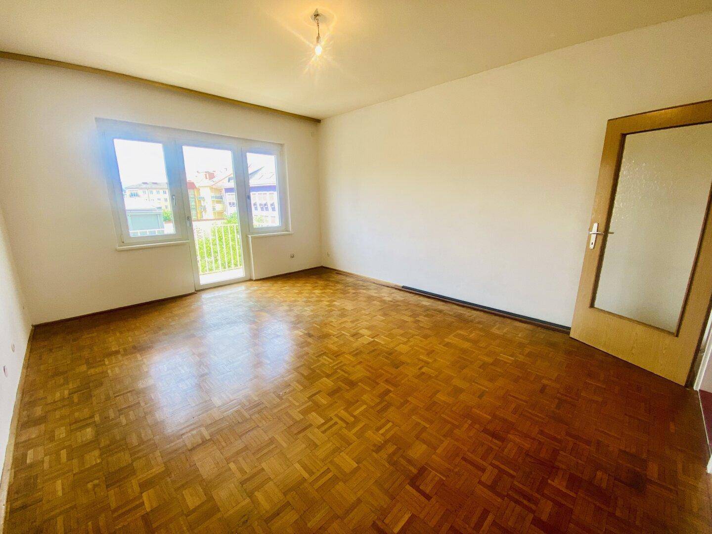Helles Wohnzimmer mit Fischgrätparkettboden und Zugang zu einem kleinen Balkon.