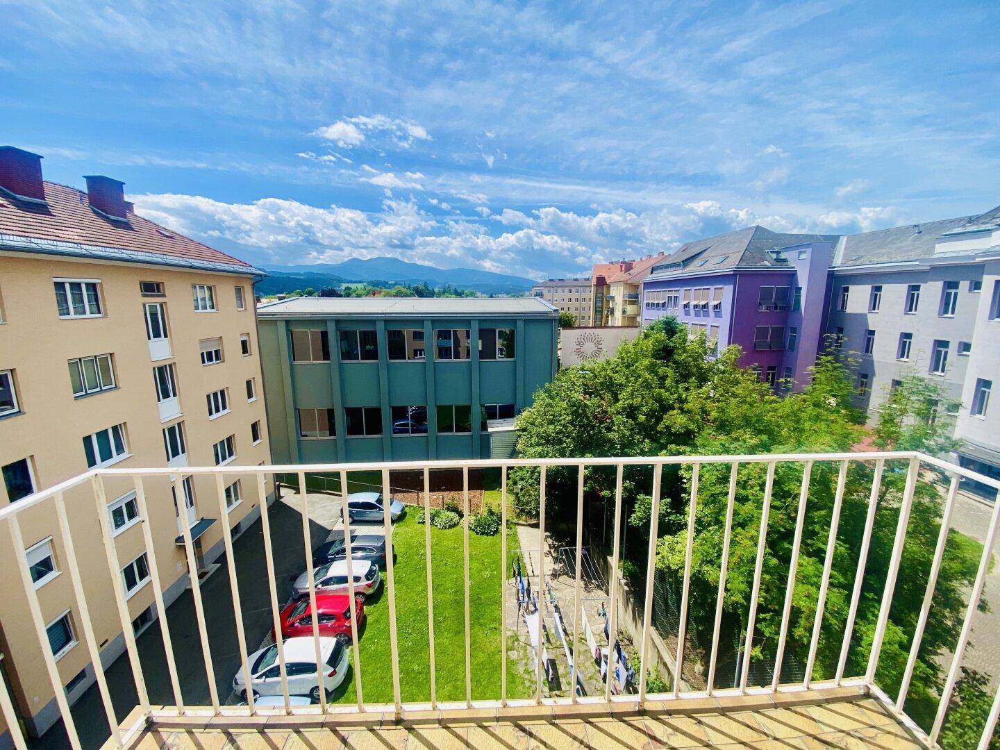 Balkon mit Blick auf den Innenhof, umliegende Gebäude und eine ferne Berglandschaft.
