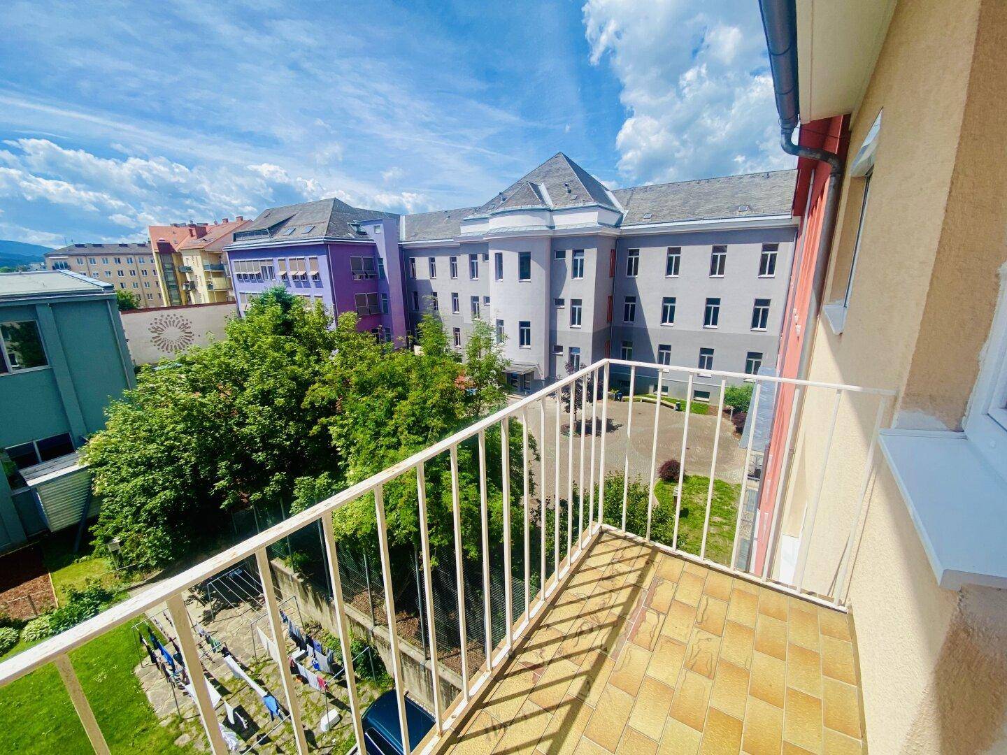 Balkon mit Blick auf einen grünen Innenhof und umliegende Wohngebäude.