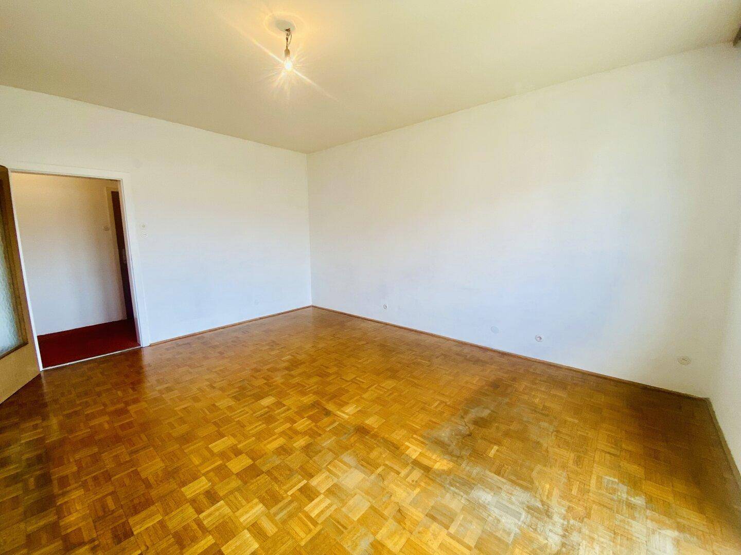 Geräumiges Wohnzimmer mit klassischem Fischgrätparkett und hellen Wänden.