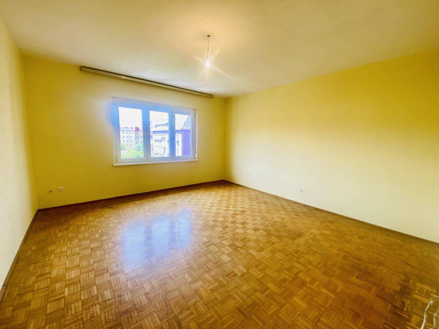 Helles Wohnzimmer mit gelben Wänden, Fischgrätparkett und großem Fenster.
