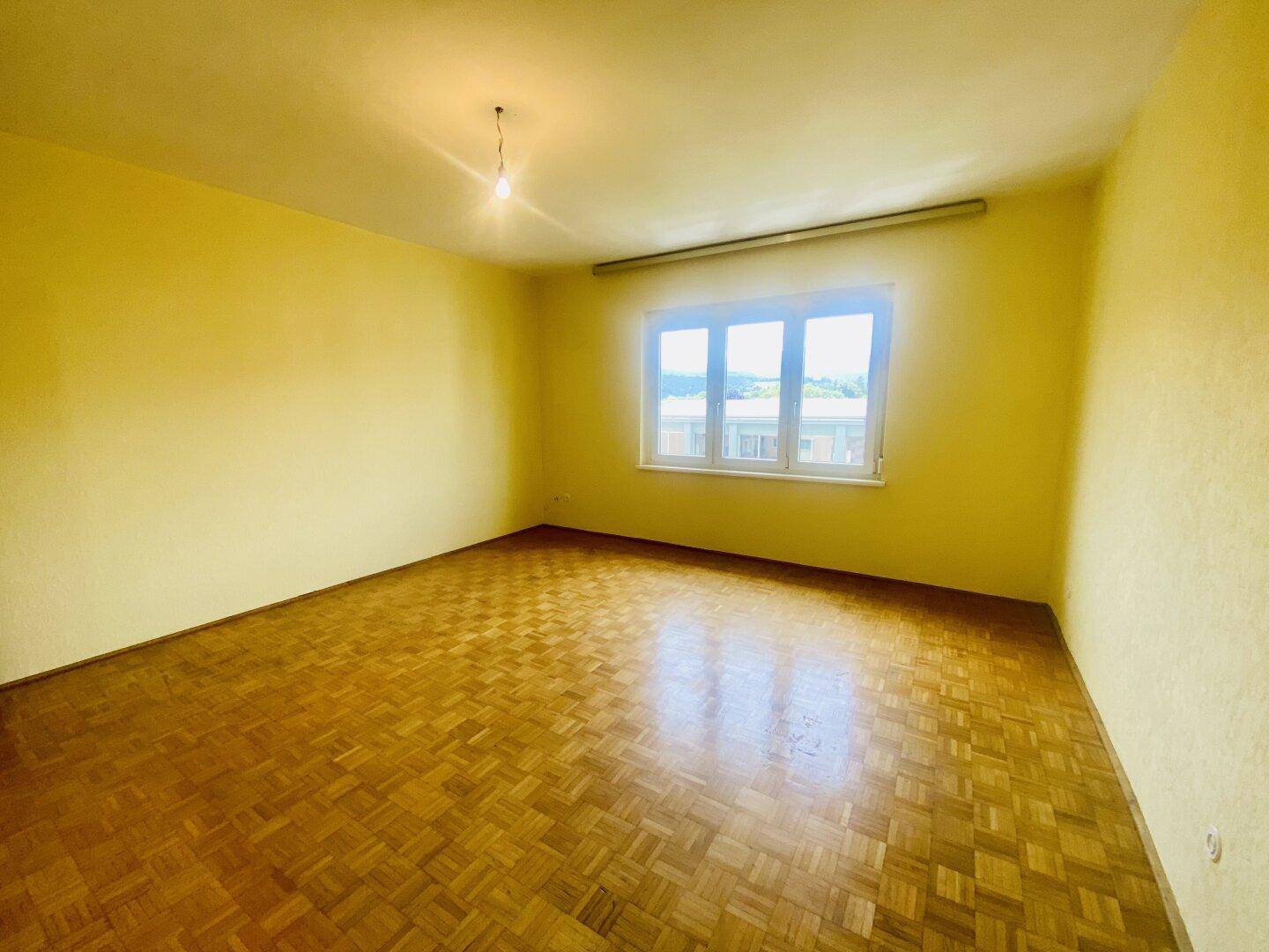 Geräumiges Wohnzimmer mit gelben Wänden, Fischgrätparkett und viel Tageslicht.