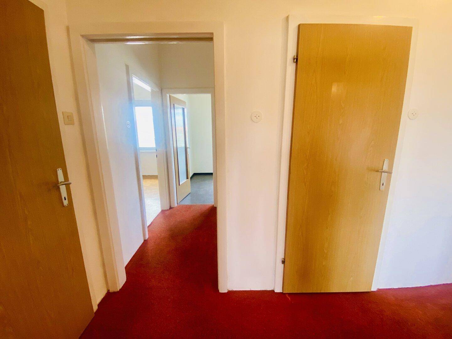 Flur mit rotem Teppichboden und Holztüren, der die verschiedenen Bereiche der Wohnung verbindet.