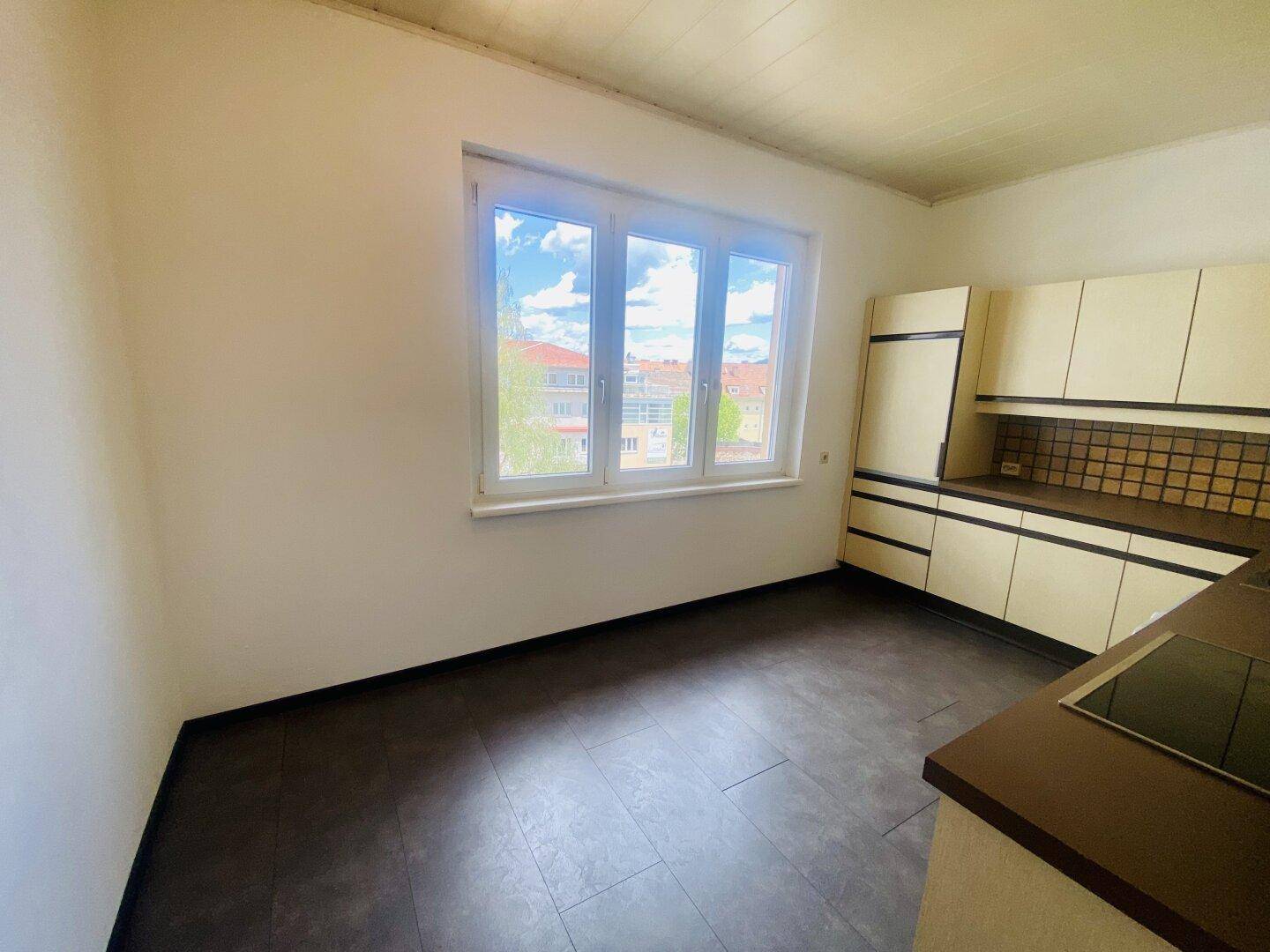 Küche mit älteren Einbauschränken, Kühlschrank und einem großen Fenster für natürliche Belichtung.