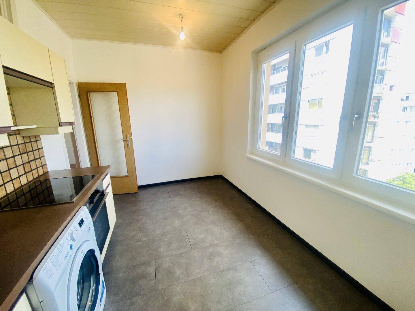 Funktionale Küche mit älteren Einbauschränken, Fliesenboden und großem Fenster.