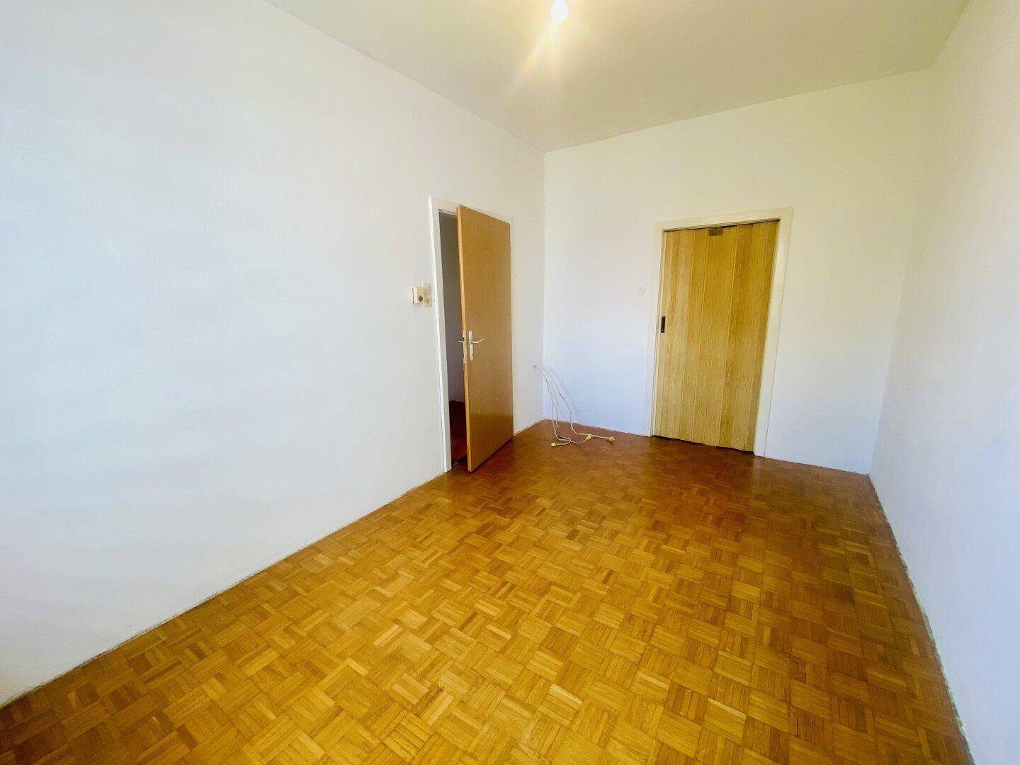 Geräumiges Schlafzimmer mit Fischgrätparkettboden und zwei Holztüren.
