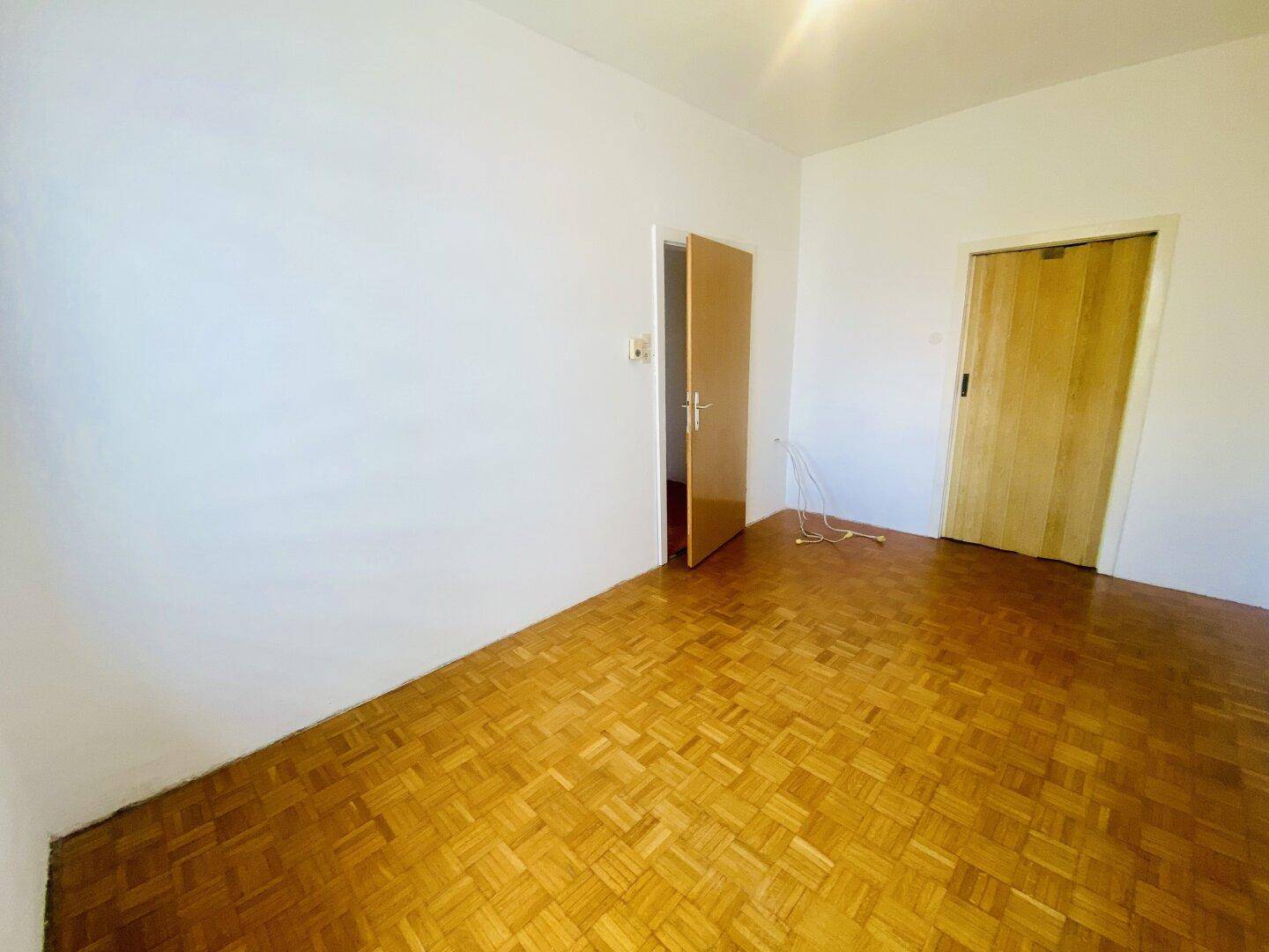 Schlafzimmer mit Fischgrätparkettboden und zwei Holztüren, bereit zur individuellen Gestaltung.