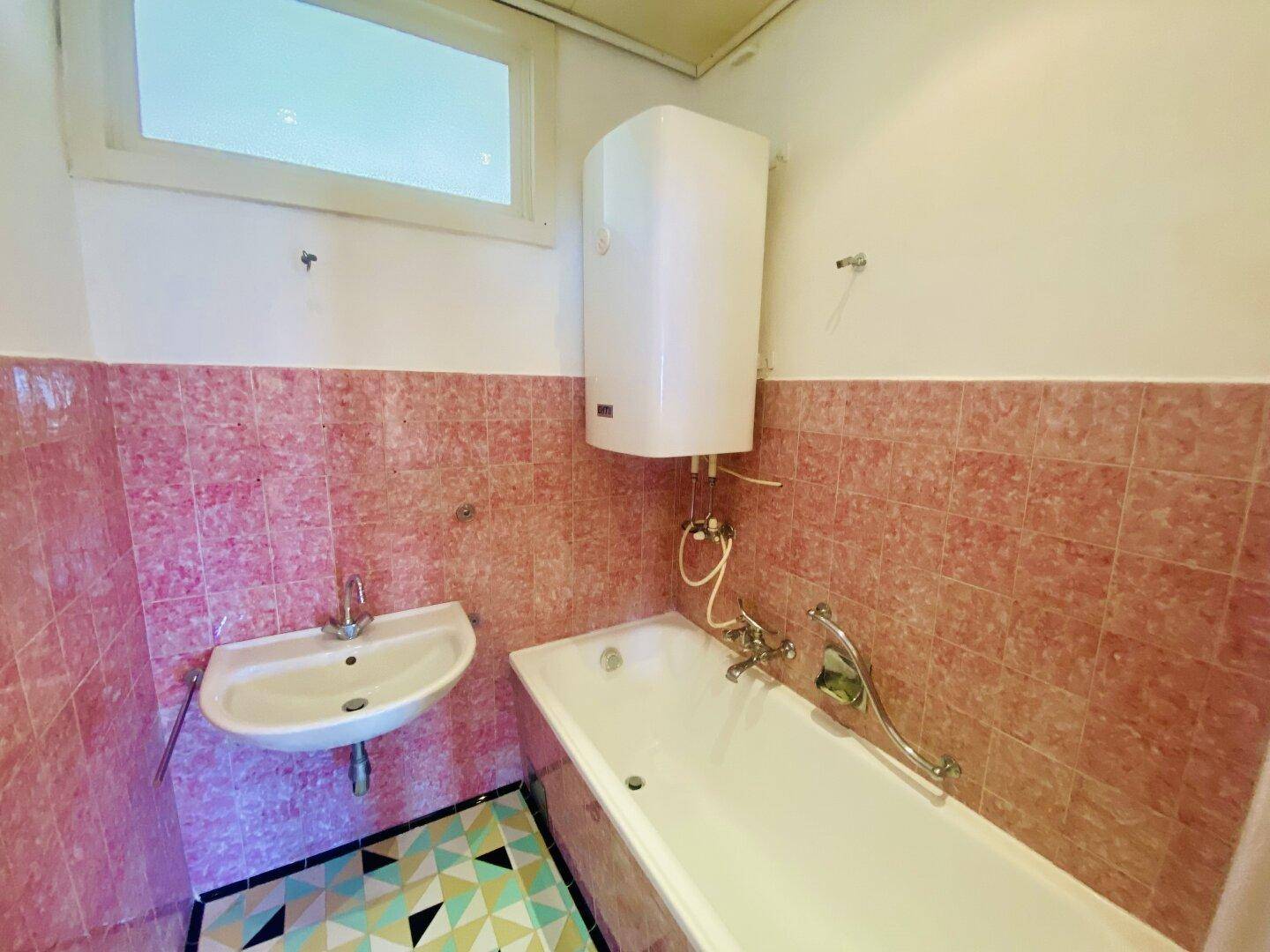 Badezimmer mit rosa Wandfliesen, Badewanne, Waschbecken und einem farbenfrohen Fliesenboden.