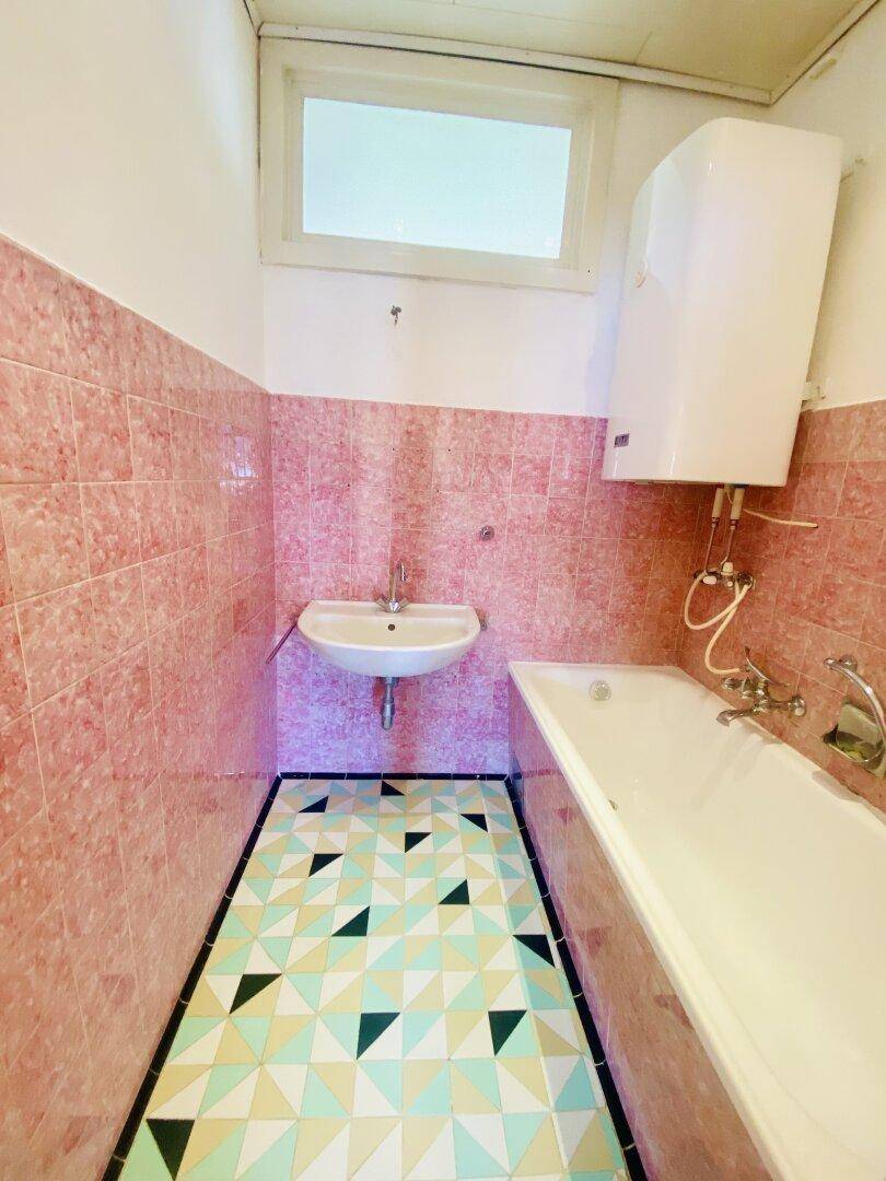 Badezimmer mit rosa Wandfliesen, geometrischem Bodenmuster und einer Badewanne.