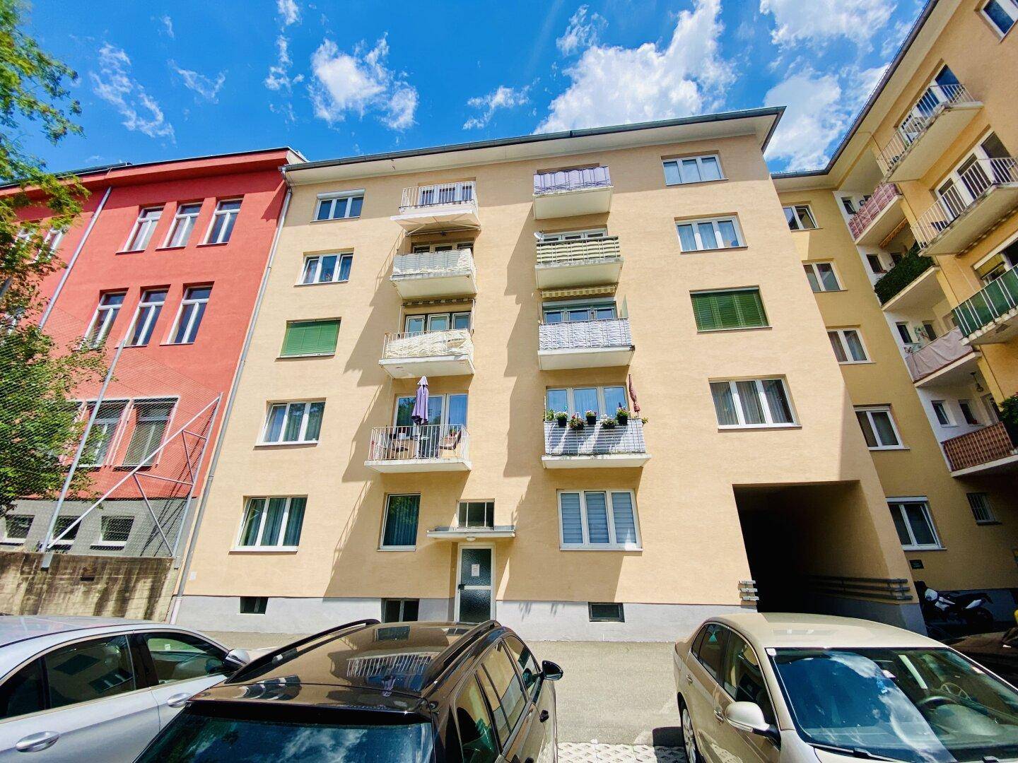 Mehrfamilienhaus mit gelber Fassade, Balkonen und parkenden Autos davor.