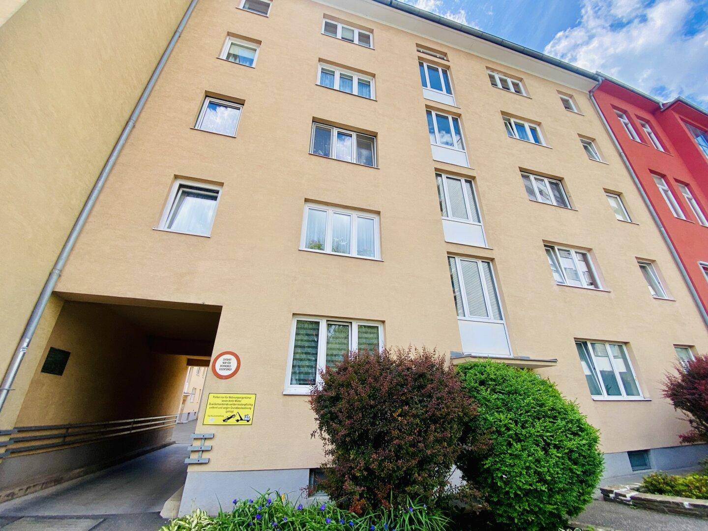 Gelbes Mehrfamilienhaus mit Zufahrt zur Tiefgarage und einer barrierefreien Rampe.