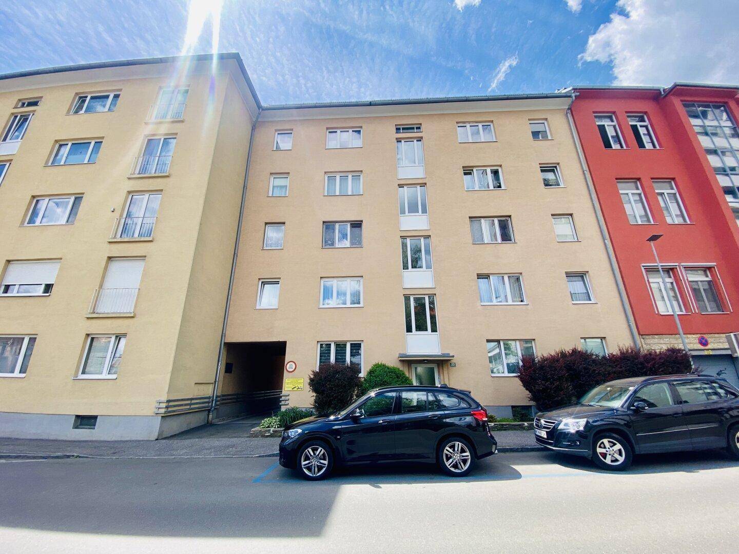 Ansicht eines gelben Mehrfamilienhauses von der Straße mit parkenden Autos.