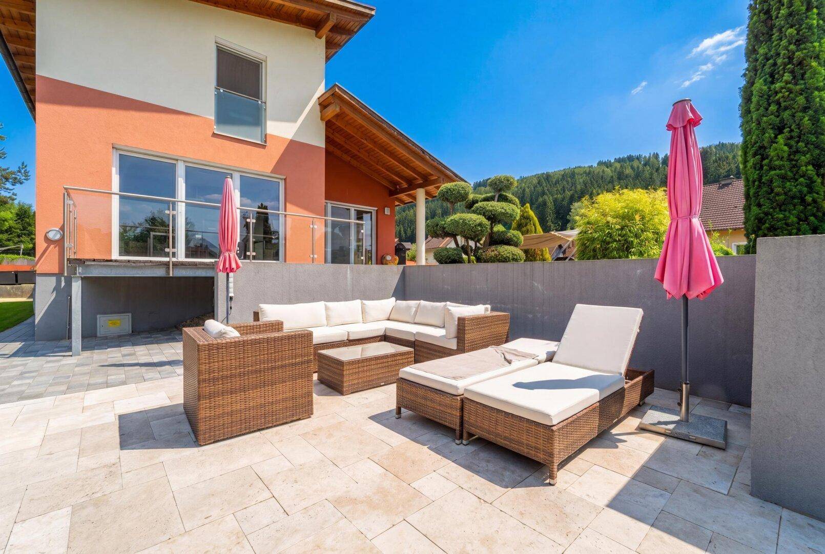 Gemütliche Sonnenterrasse mit Rattanmöbeln und großem Sonnenschirm, ideal zum Entspannen.