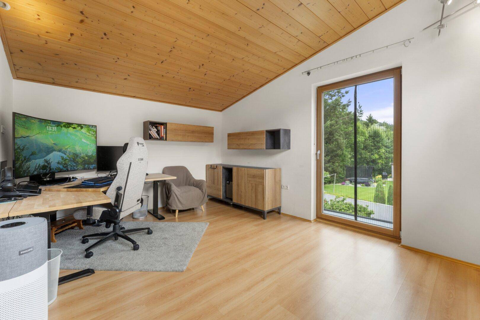 Helles Arbeitszimmer mit Holzdachschräge, großem Fenster und Blick ins Grüne.