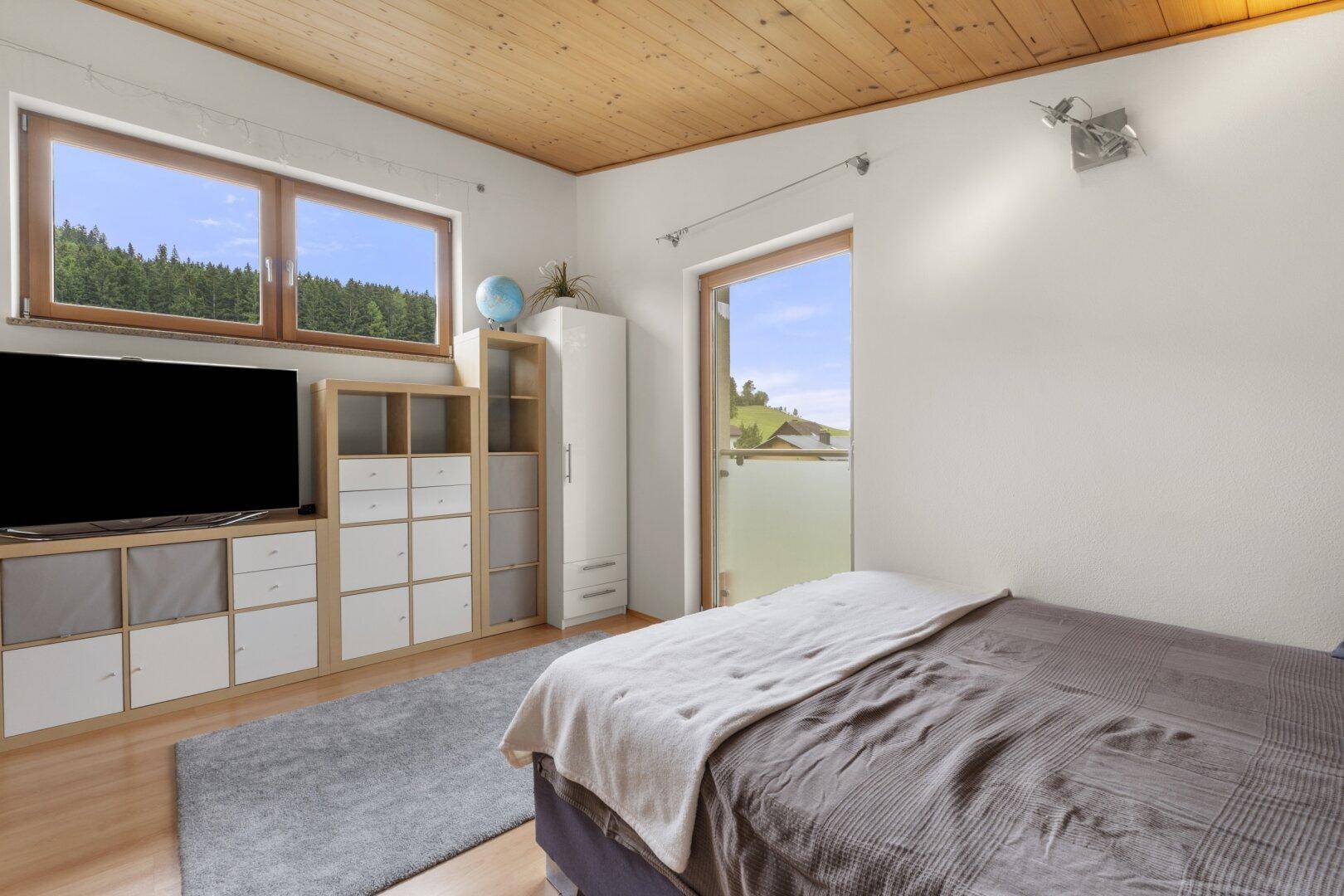 Gemütliches Schlafzimmer mit Holzdachschräge, großem Bett und Blick auf die Landschaft.