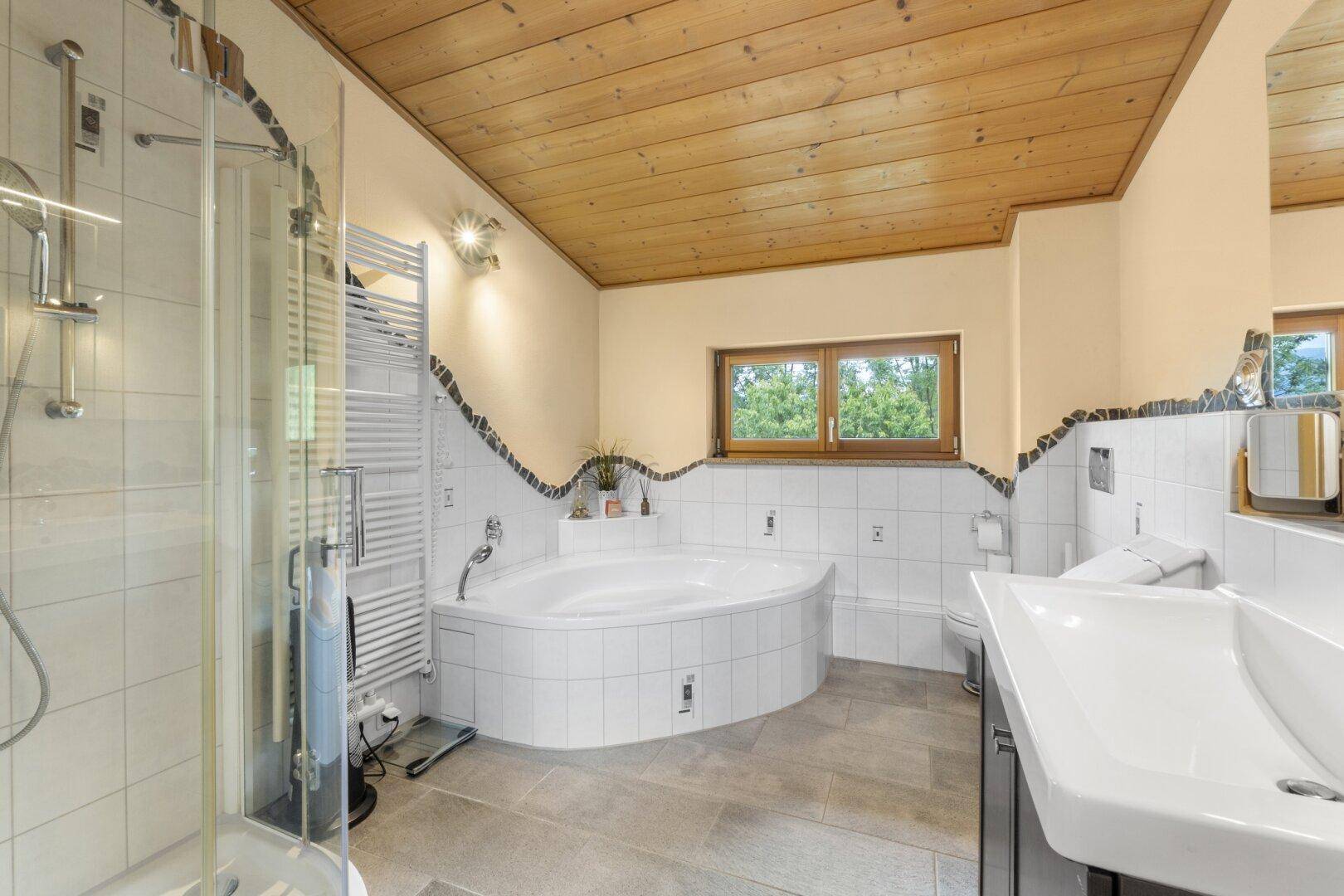 Geräumiges Badezimmer mit Eckbadewanne, separater Dusche und Fenster mit Blick ins Grüne.