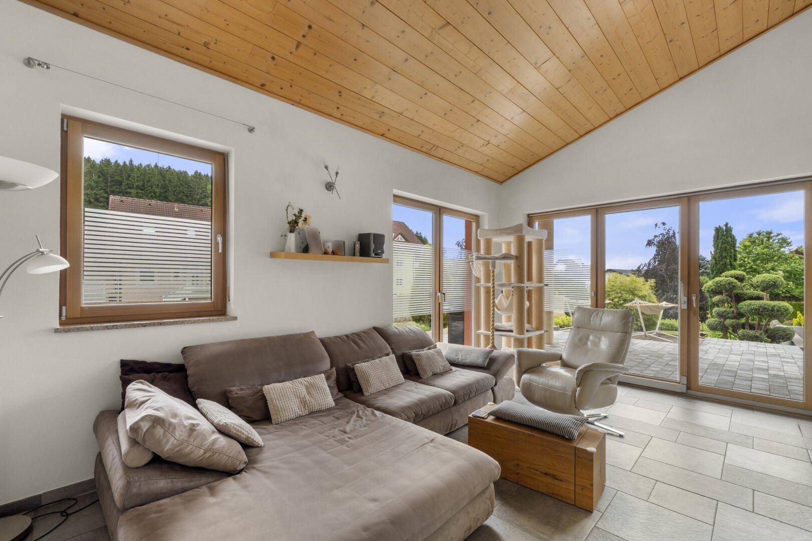 Helles Wohnzimmer mit bequemer Couch, Holzdachschräge und großen Fenstern zum Garten.