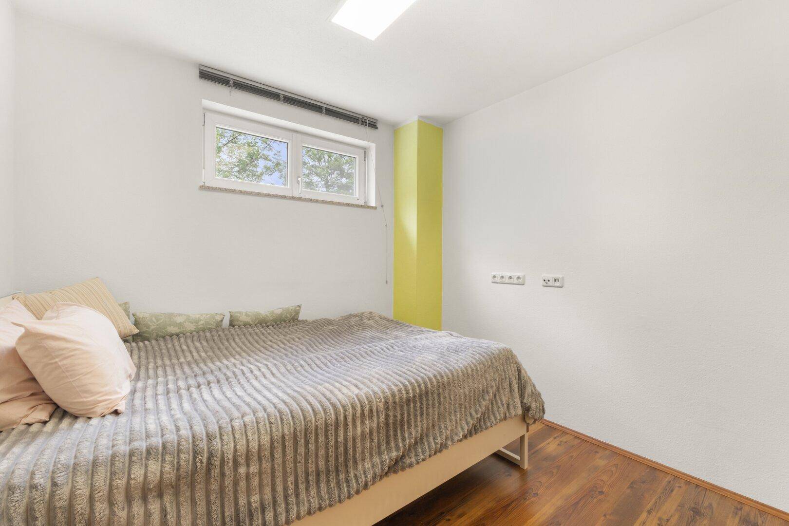 Helles Schlafzimmer im Untergeschoss mit Fenster und Holzboden.