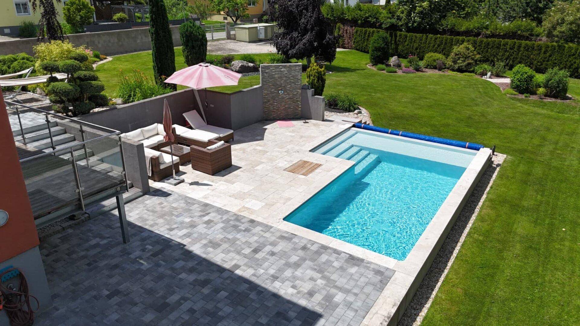 Moderner Swimmingpool mit breiter Treppe und angrenzender Sonnenterrasse im gepflegten Garten.