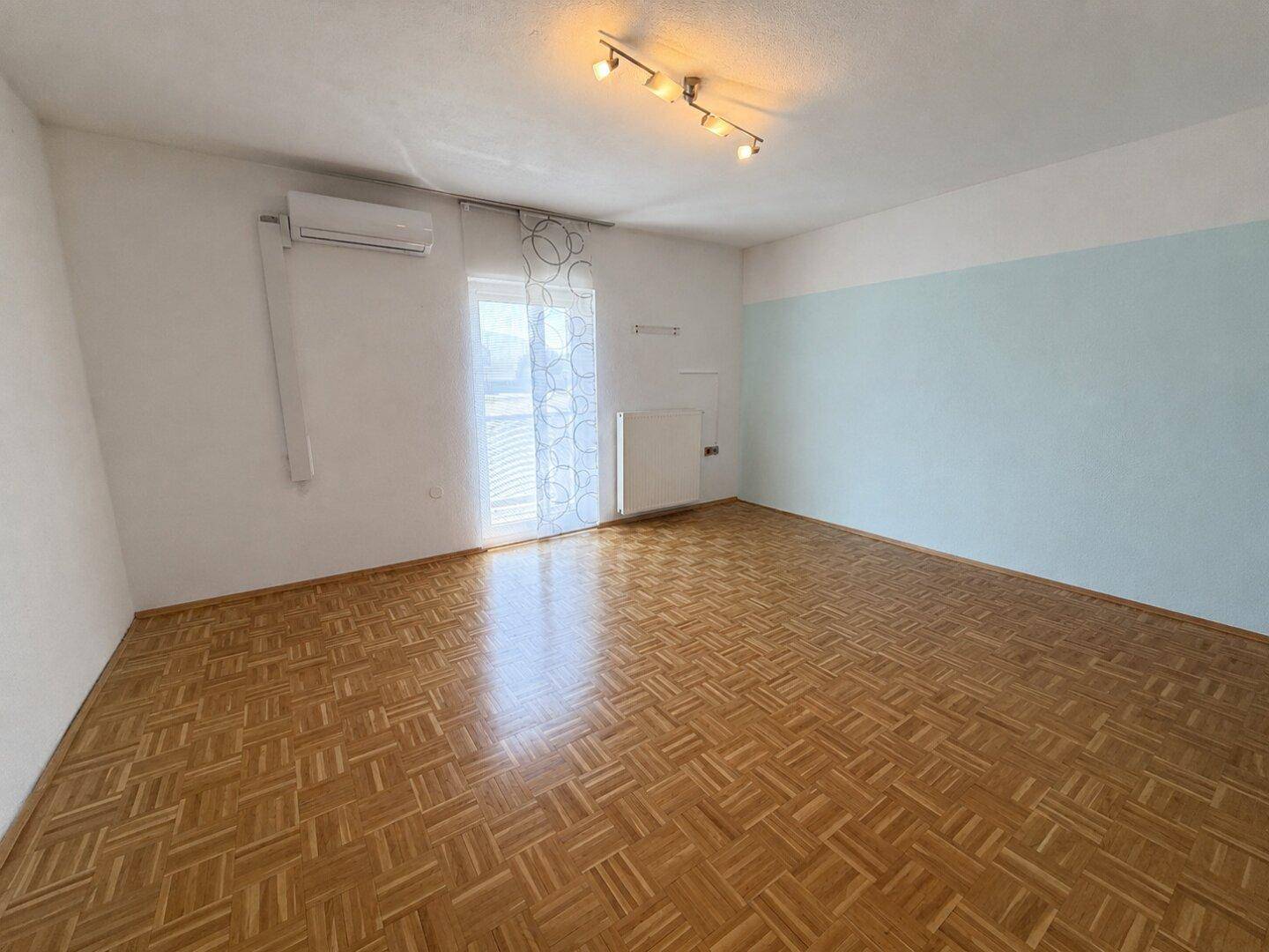Geräumiges Wohnzimmer mit Parkettboden, Klimaanlage und großem Fenster für viel Tageslicht.