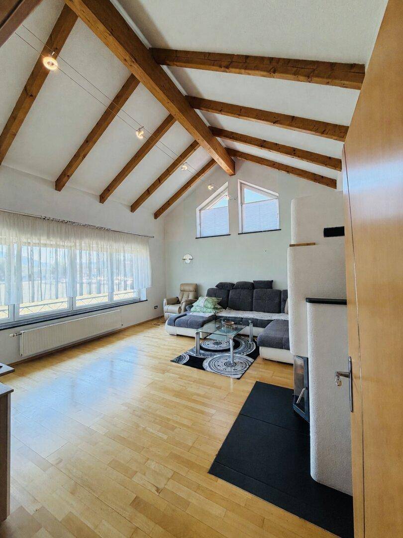 Helles Wohnzimmer mit Holzbalken, Kamin und großen Fenstern mit Weitblick ins Grüne.