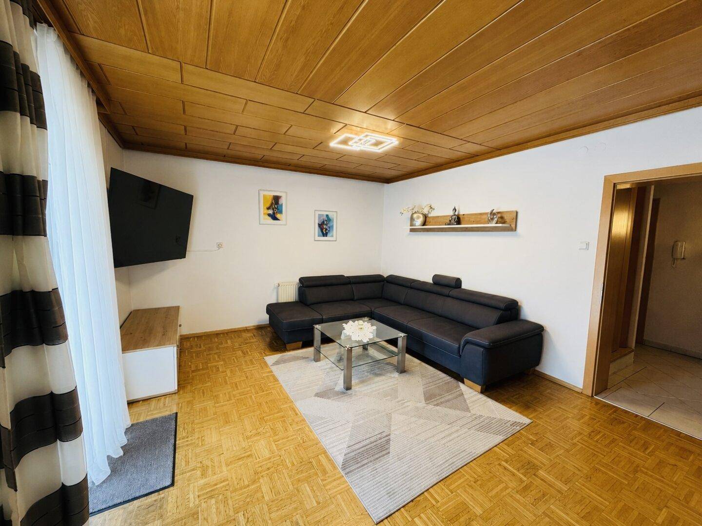 Gemütliches Wohnzimmer mit Holzkassettendecke, Ecksofa und Parkettboden.