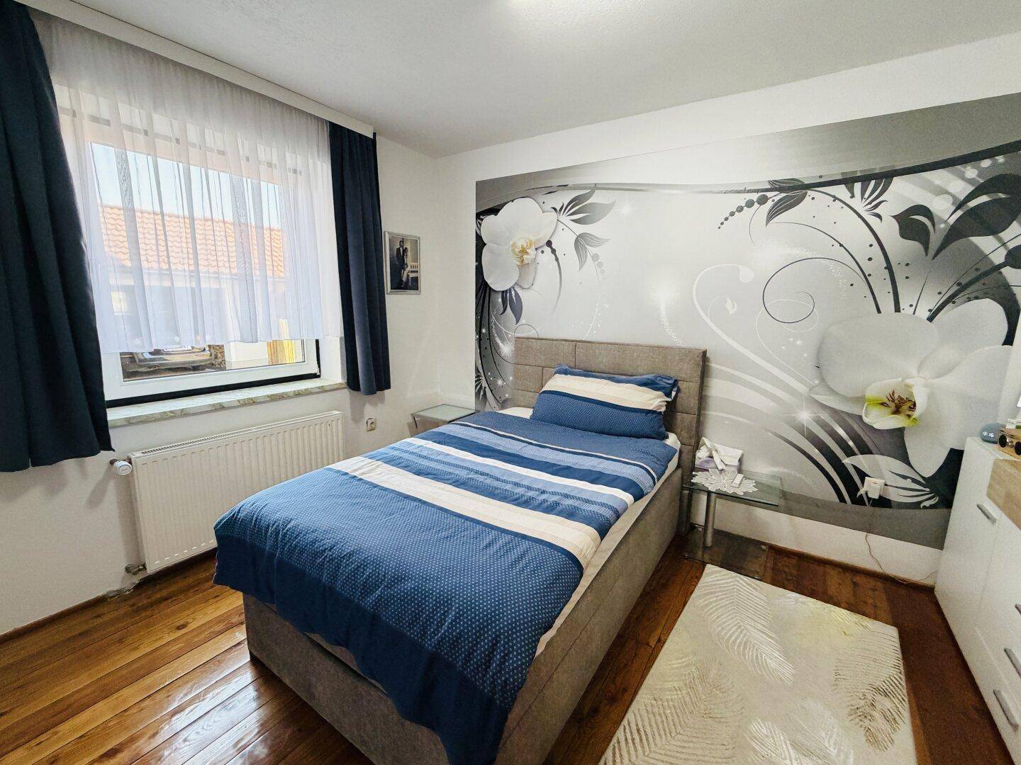 Schlafzimmer mit Einzelbett, Holzboden und dekorativer Wandtapete.