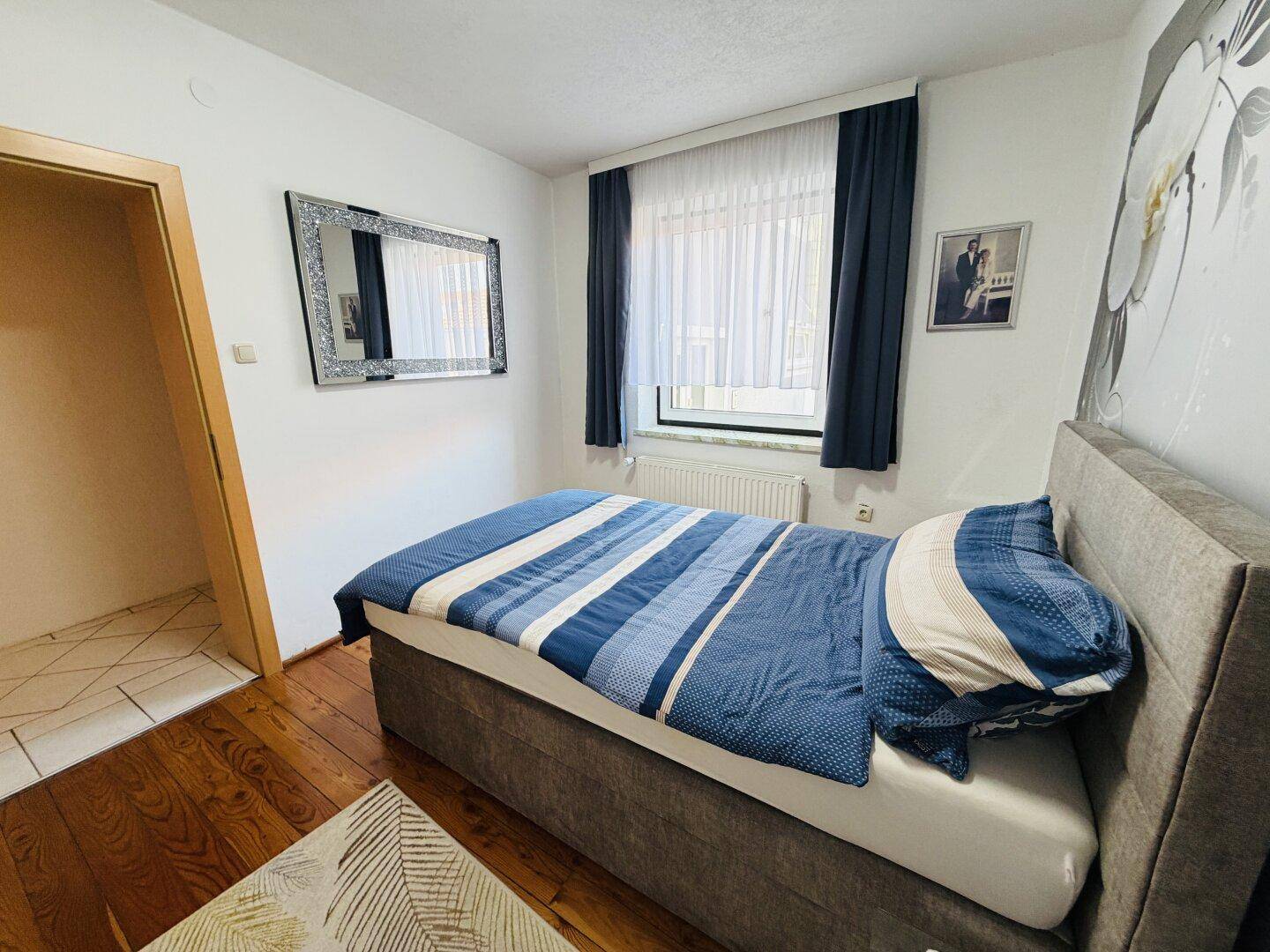 Helles Schlafzimmer mit Holzboden, Fenster und modernem Spiegel.